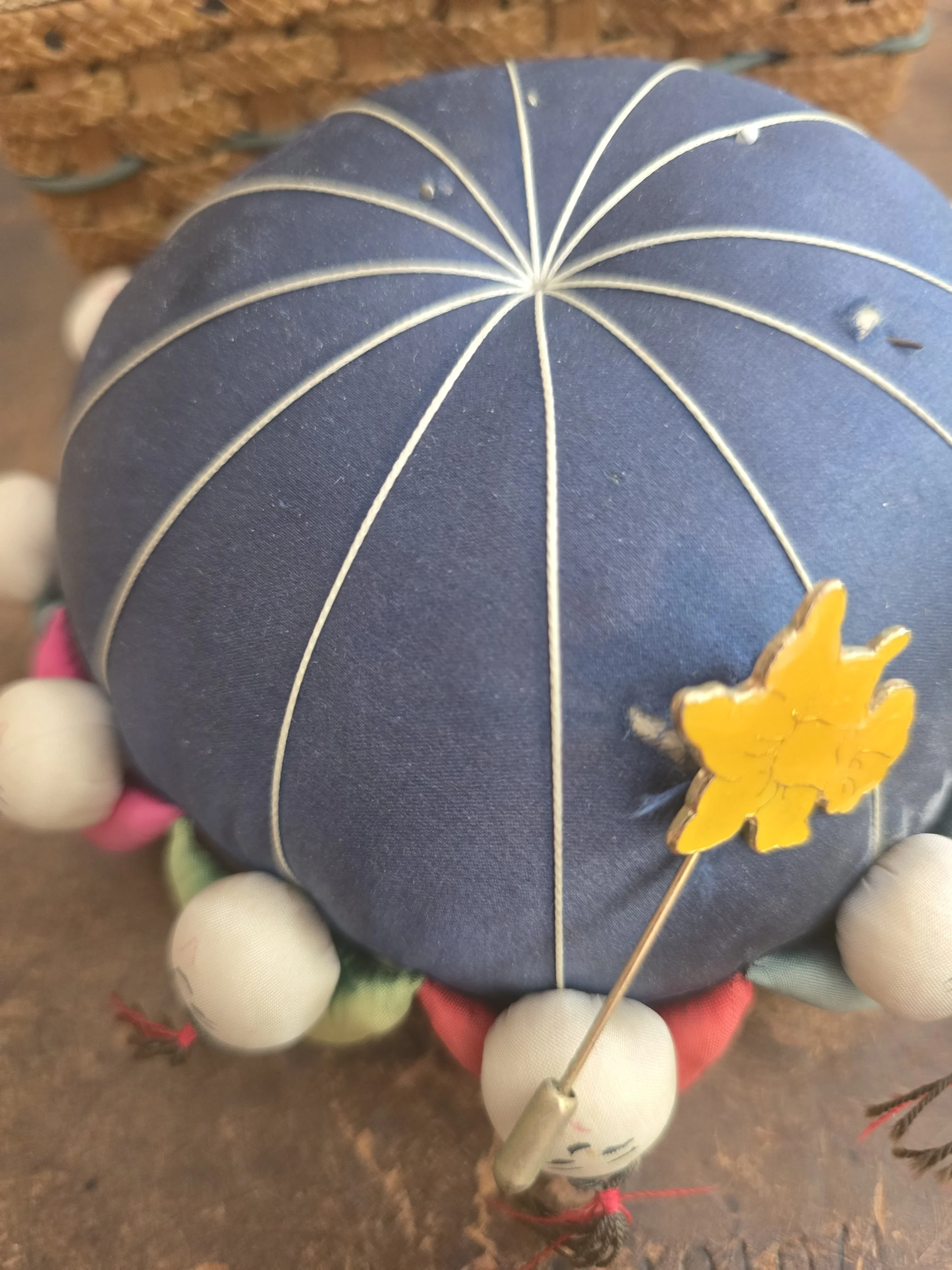 Timeworn pin cushion with painted doll heads and colourful fabric trim.