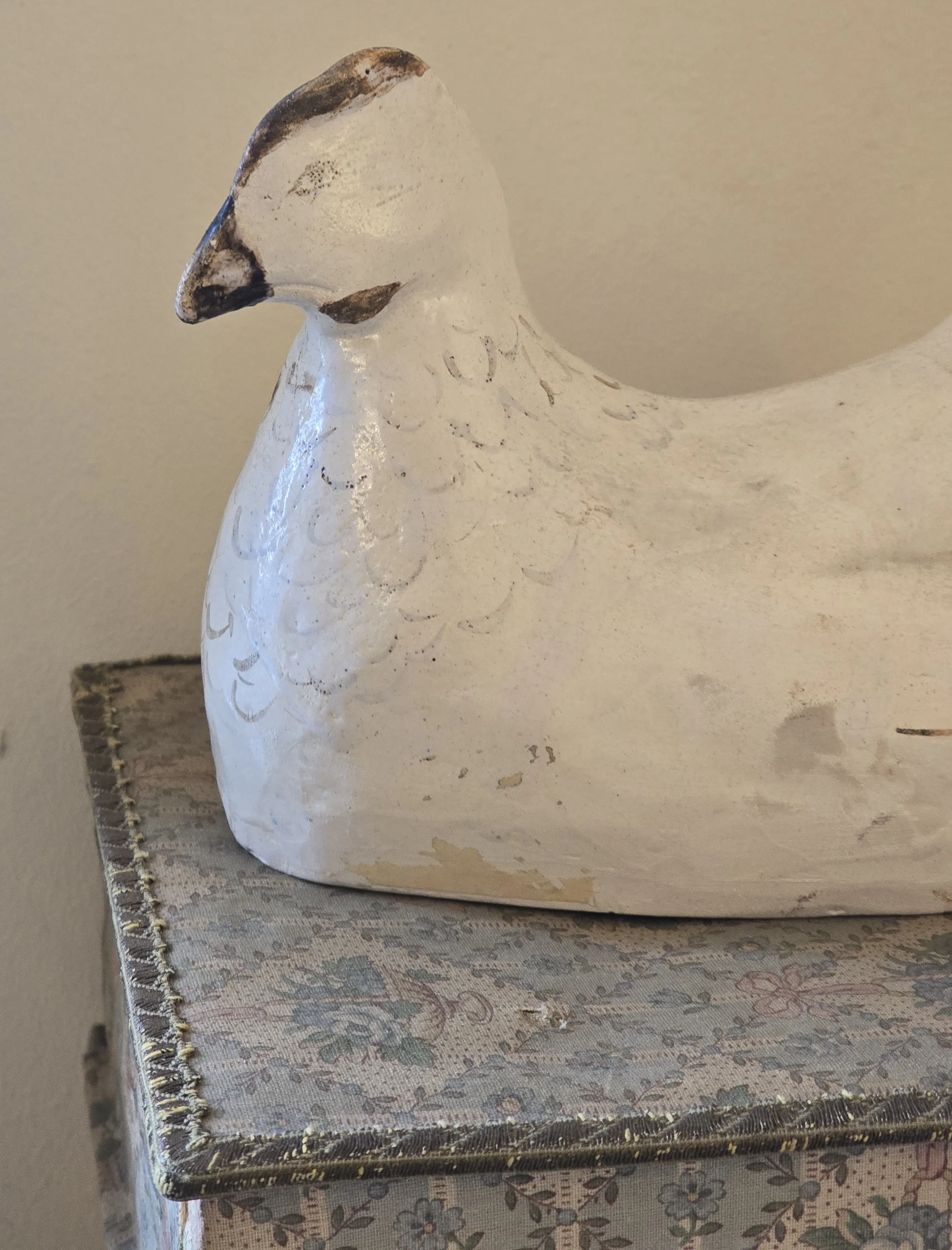 Side view of old painted hen showing timeworn white surface, faded decoration and areas of paint loss.