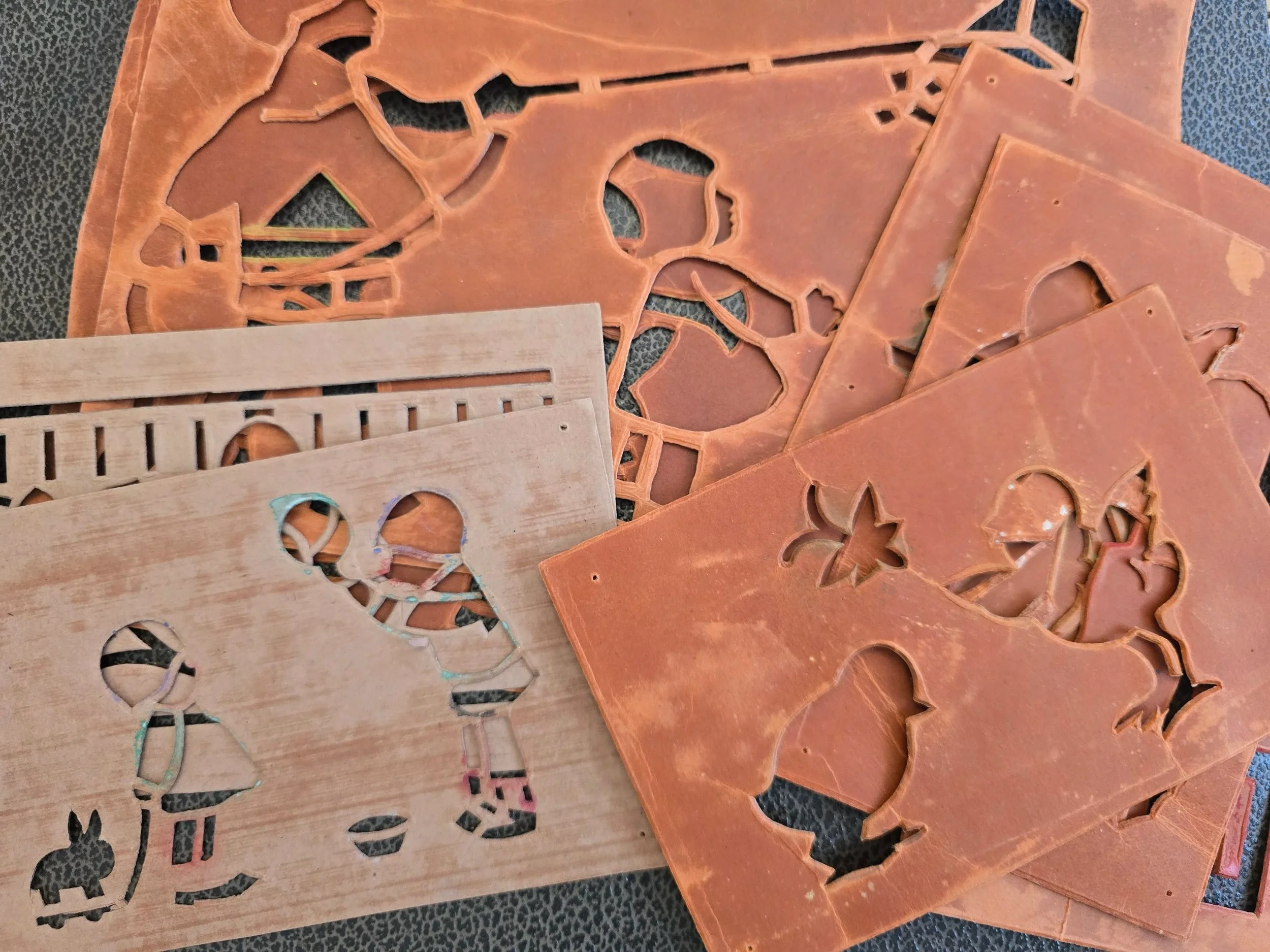 Collection of vintage terracotta-red card stencils with cut-out birds, flowers and decorative motifs, showing age and wear.