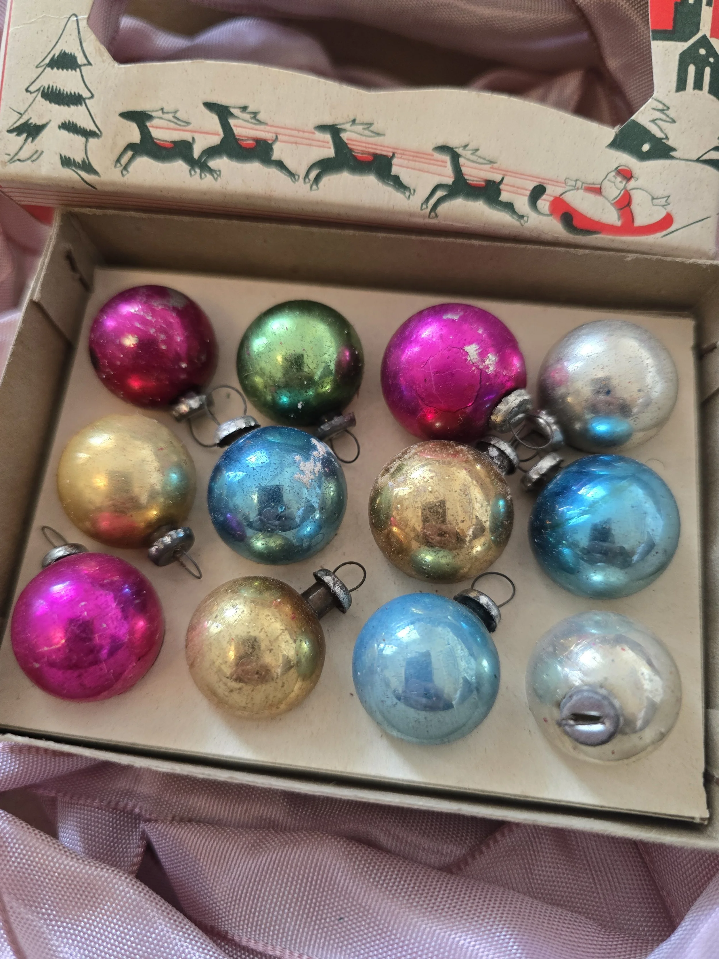Twelve small vintage glass Christmas baubles in pink, blue, green, gold and silver, displayed in their original box.