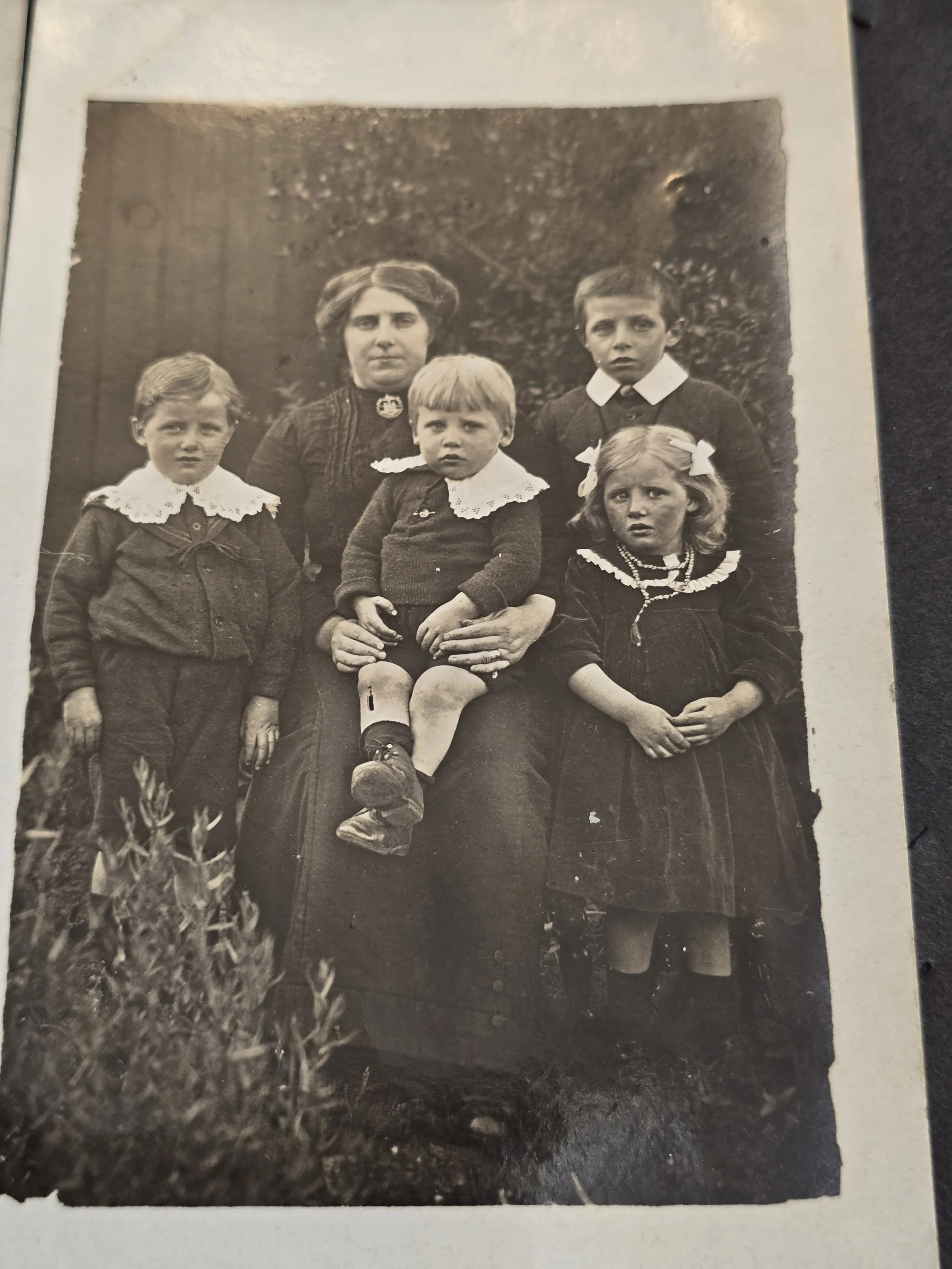 Antique photographic postcard showing an elderly woman holding hands with two young children.