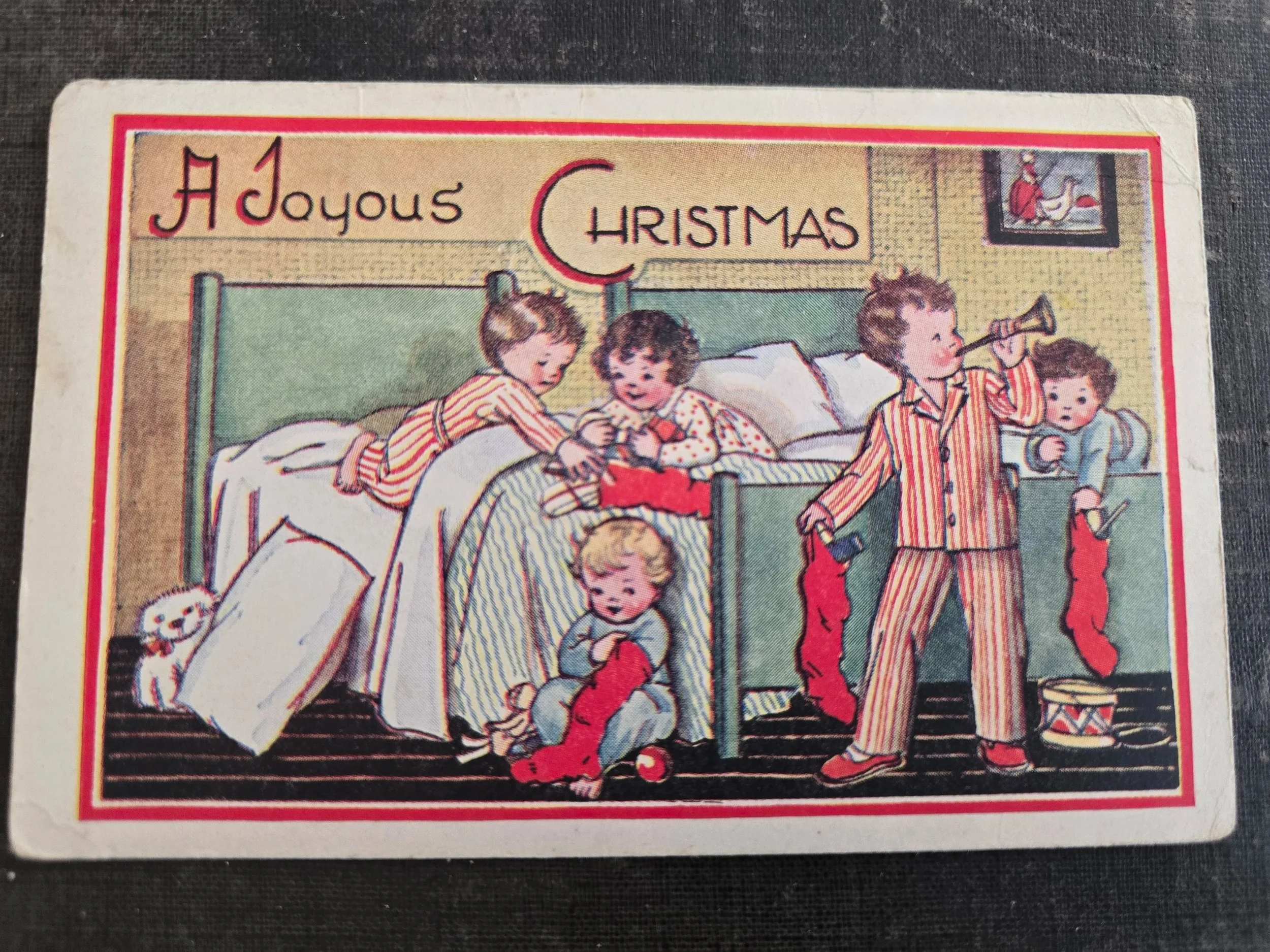 Vintage A Joyous Christmas postcard showing children in striped pyjamas playing with toys and Christmas stockings.