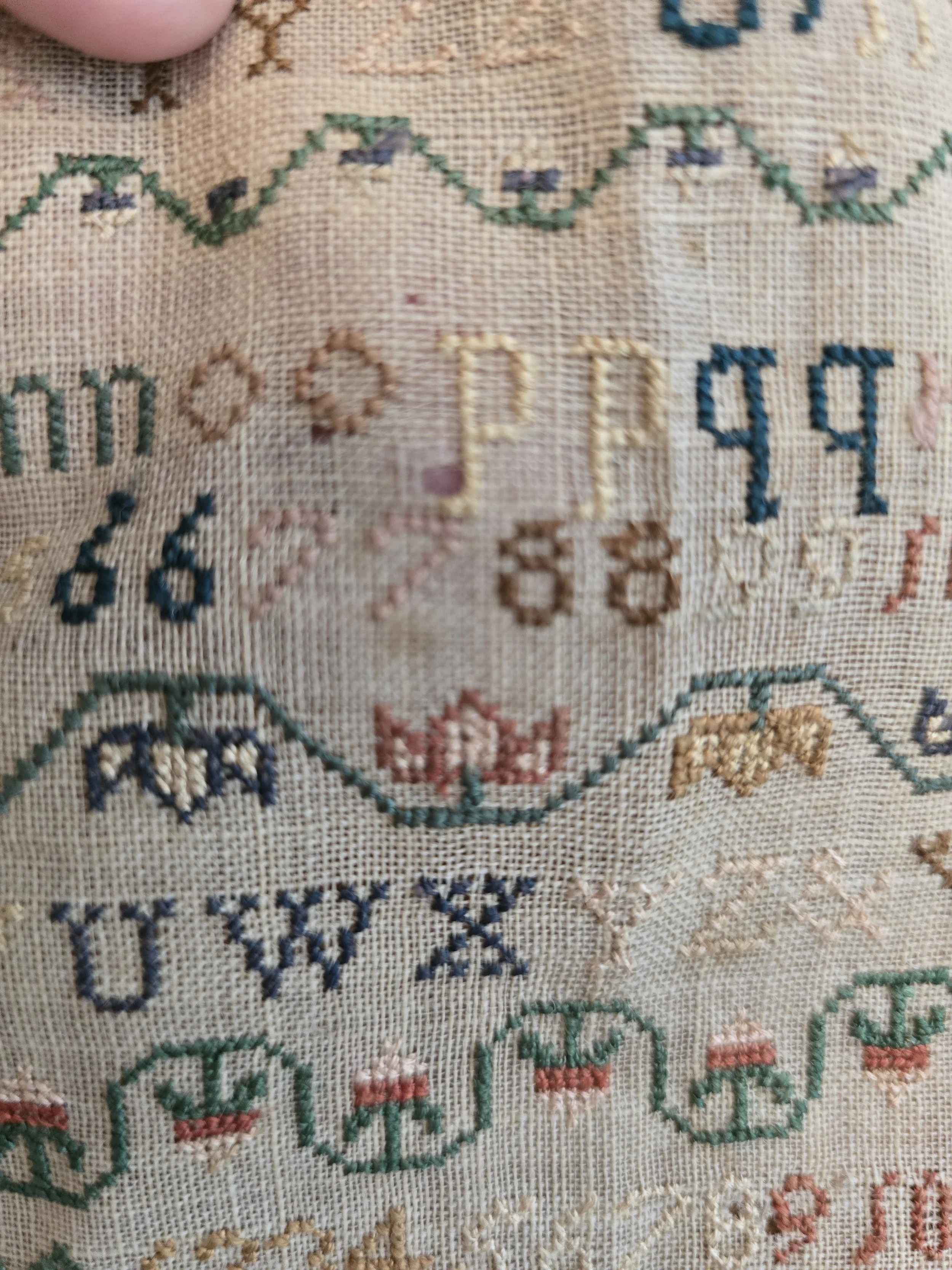 Detail showing original hand stitched alphabet rows in faded blue, green and pink threads.