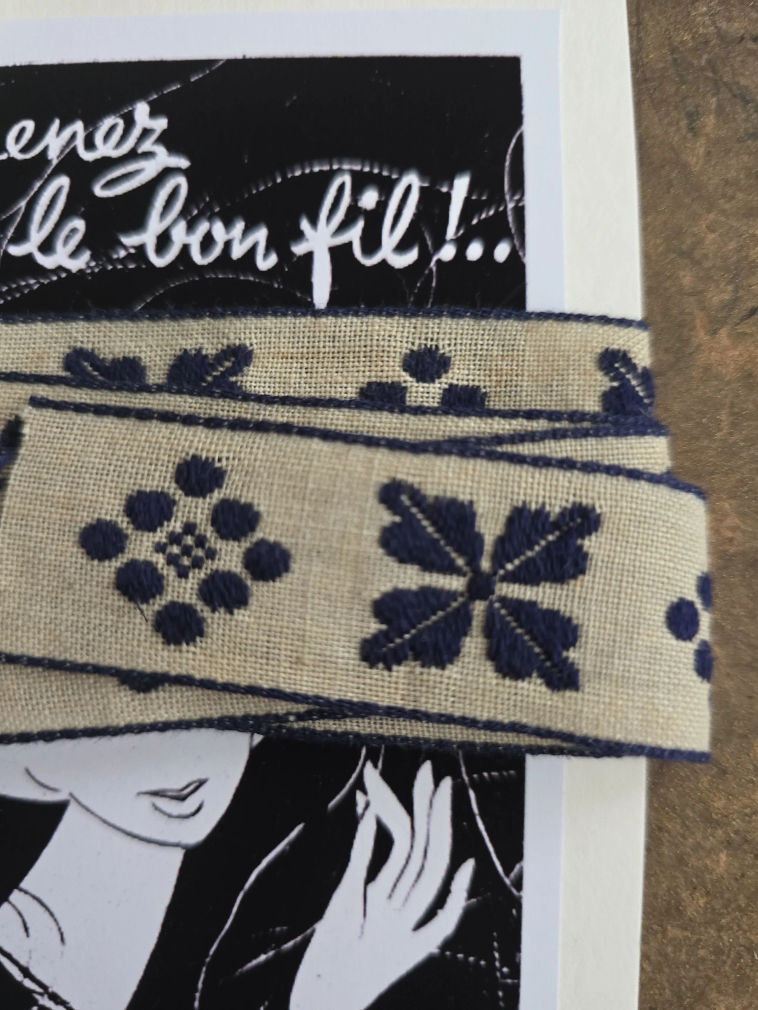 Vintage haberdashery trim with navy floral and geometric motifs on an aged cream ground.