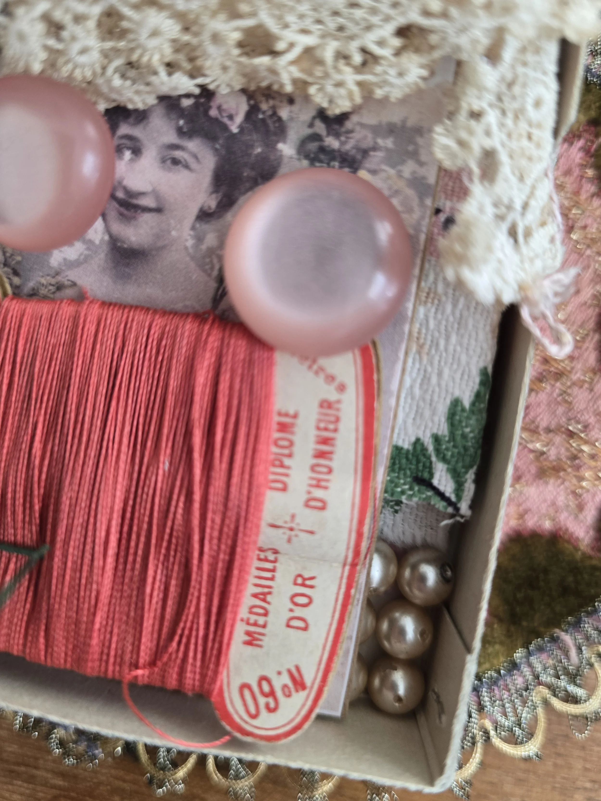 Close-up of a handmade card featuring two vintage pink buttons alongside French embroidery thread and early twentieth century lace.