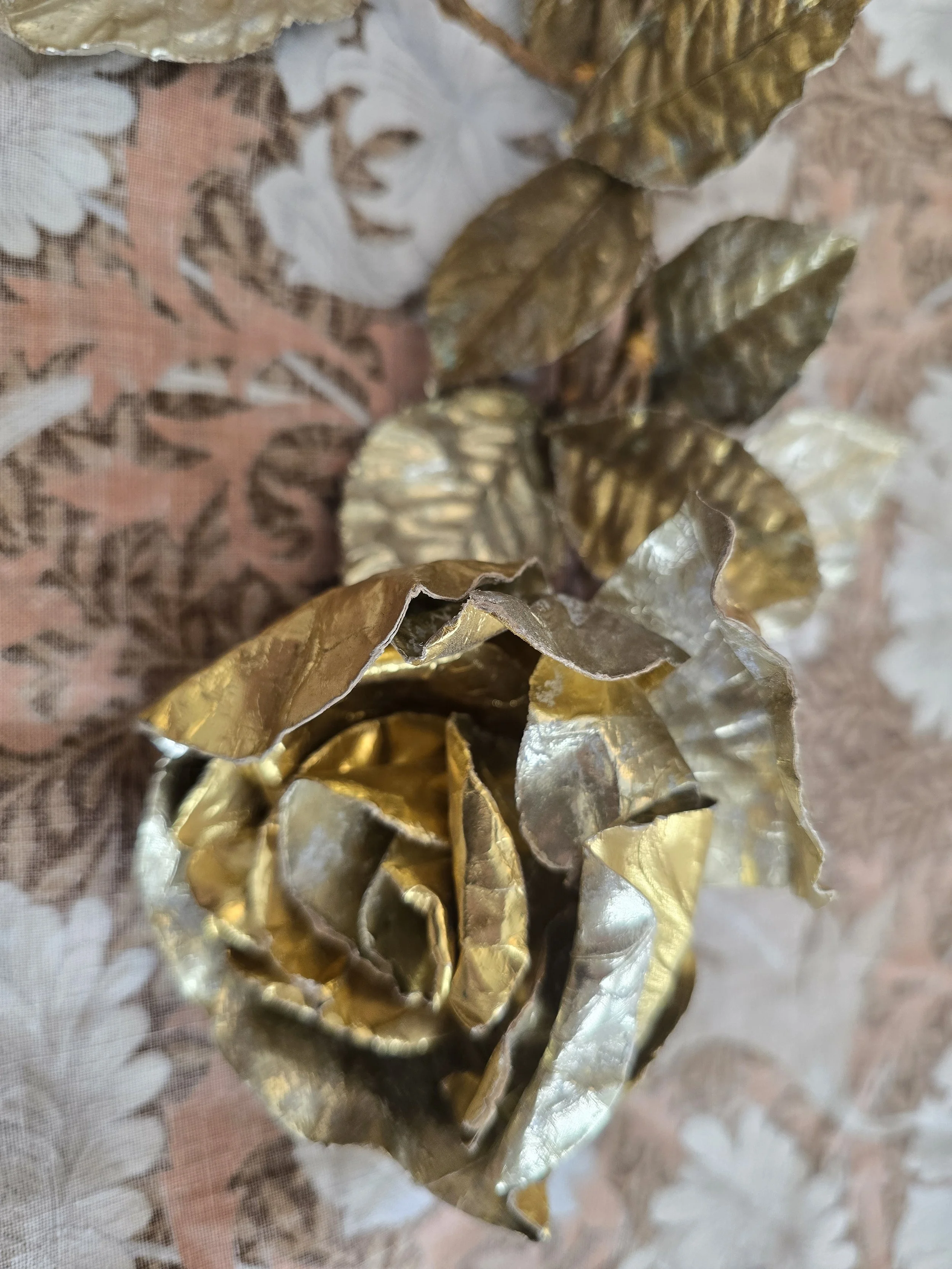 Vintage decorative gold rose stem with embossed metallic leaves and aged patina.