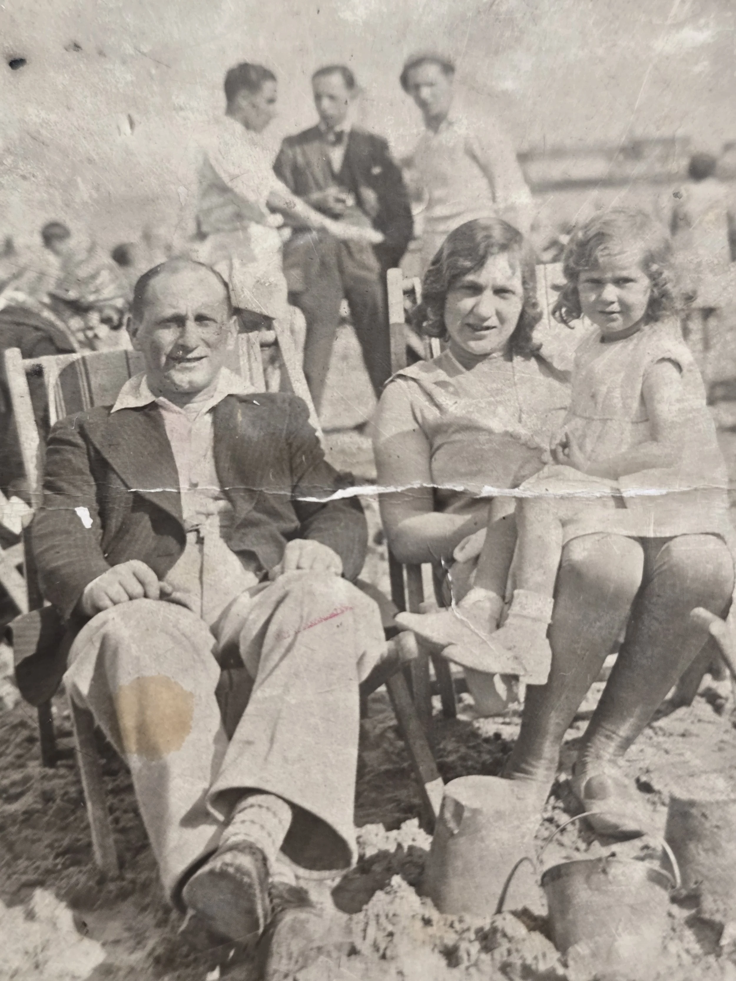 Close-up of man seated in a deckchair in a faded and heavily creased 1930s seaside photograph.