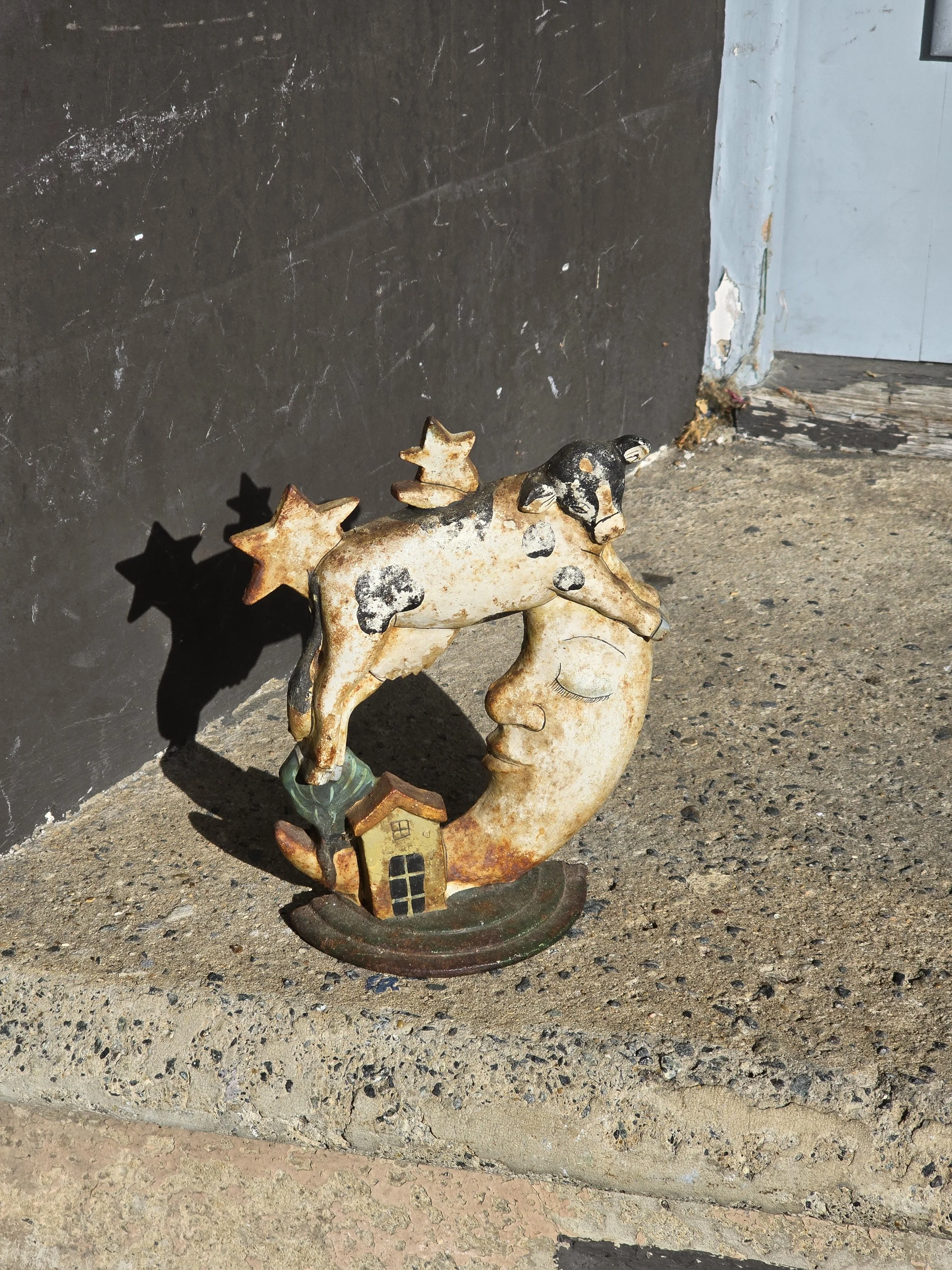 Close-up of the vintage cow and crescent moon ornament showing heavily aged paint, rust and hand-drawn facial details.