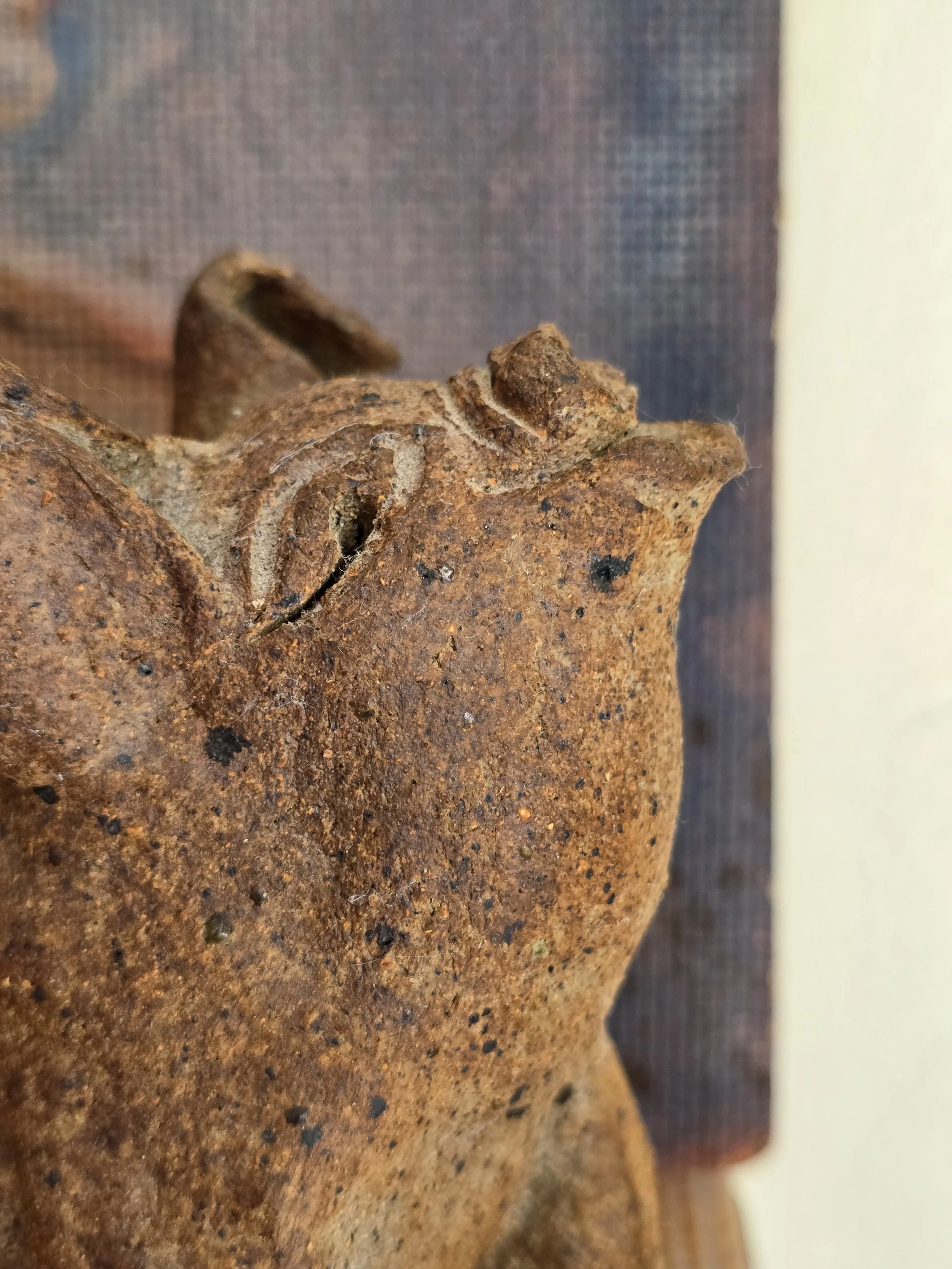 Side view of rustic studio pottery pig showing pointed ears, raised snout and textured clay surface