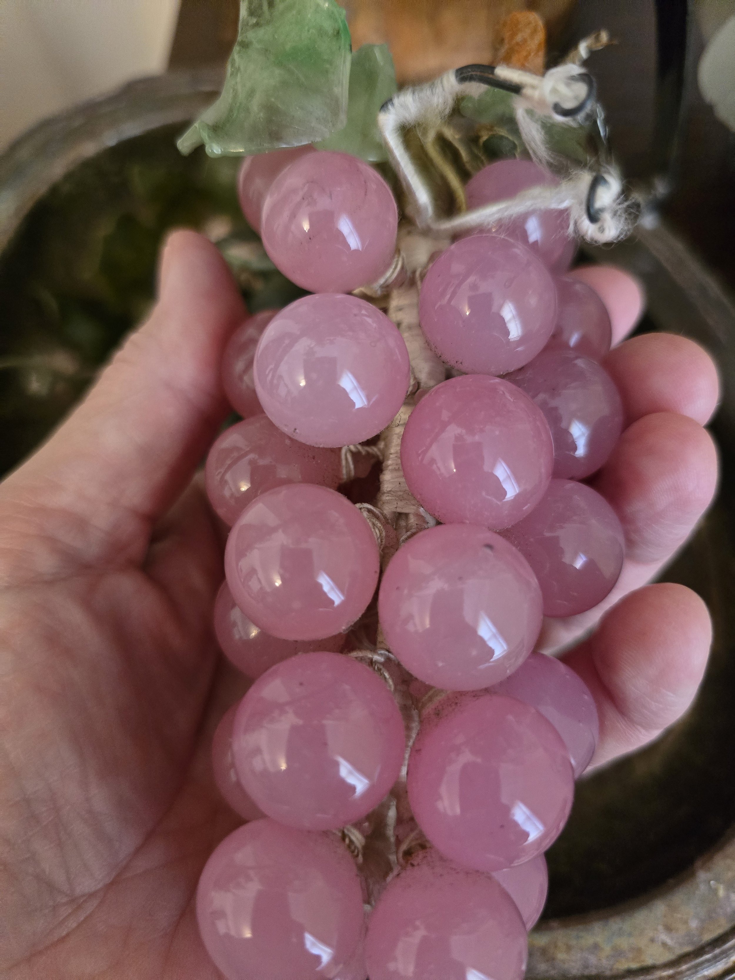 Vintage pink glass grape cluster held in hand showing its size, glass leaves and wrapped stems.