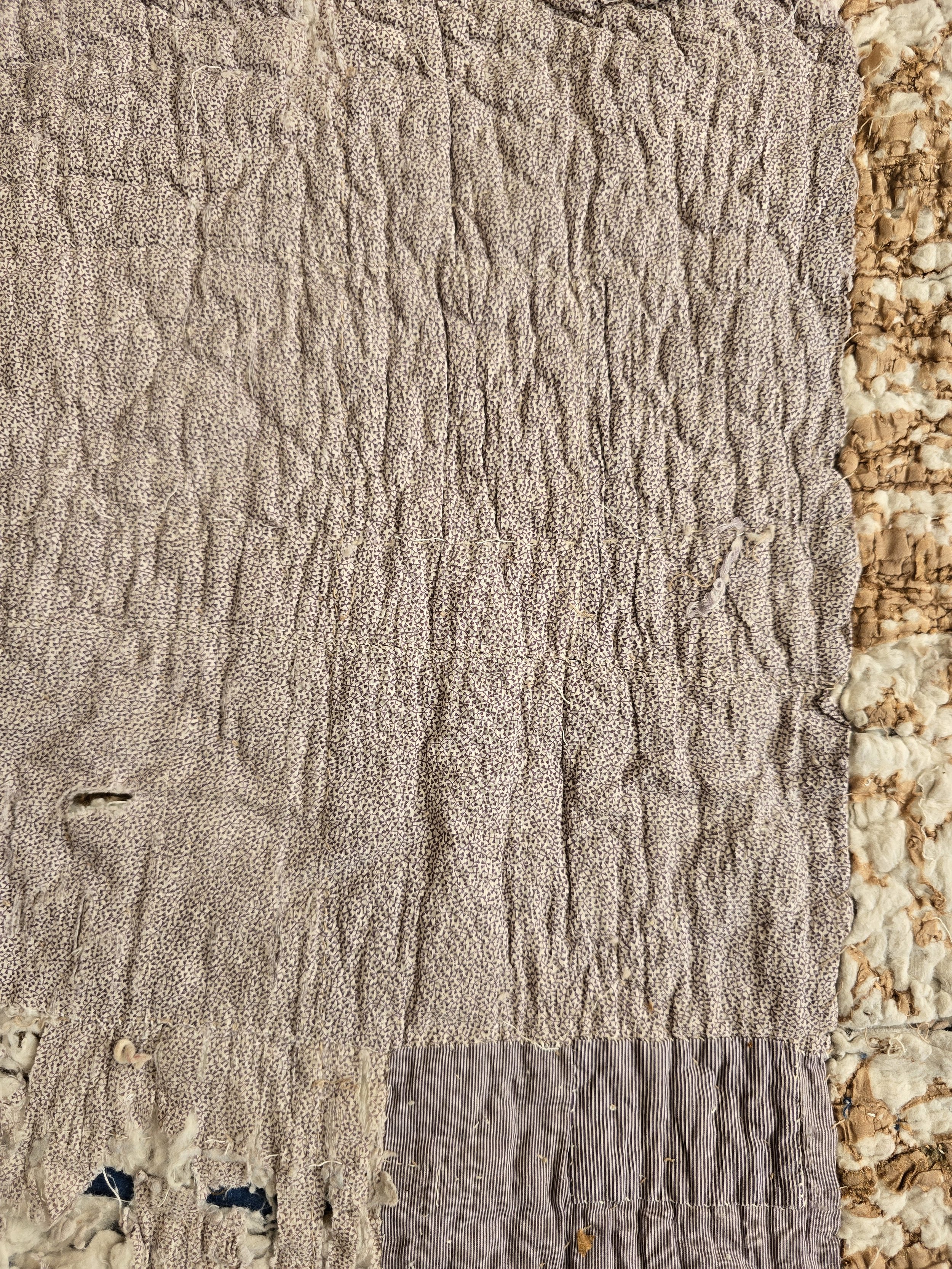 Antique quilt fragment with small purple striped cotton repair hand stitched onto faded printed fabric.