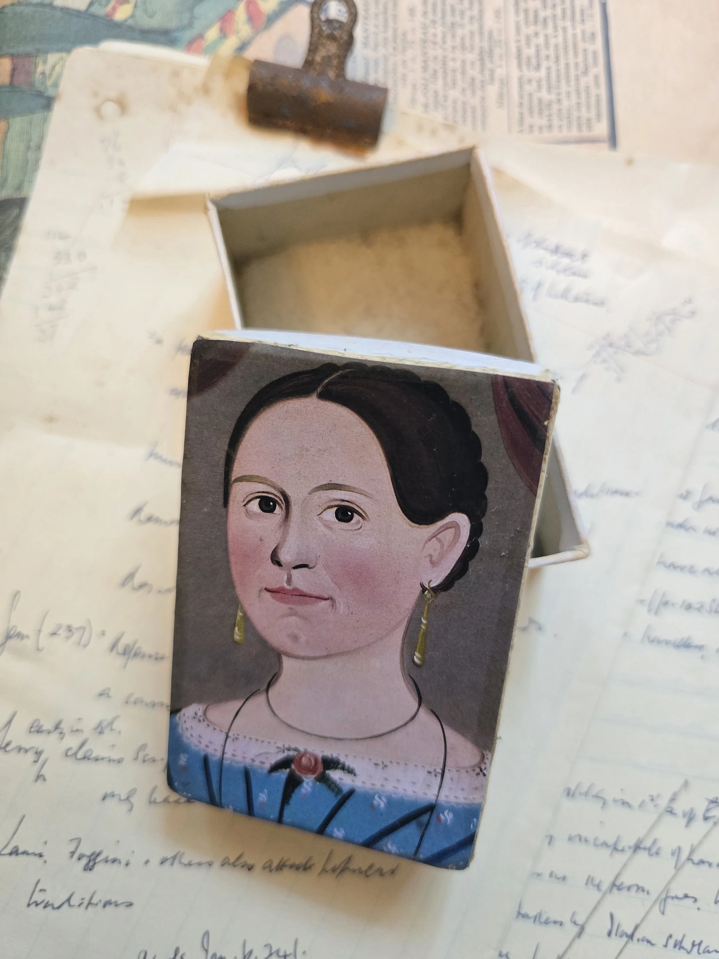 Small vintage portrait box open to show its aged cream interior and decorated portrait lid.
