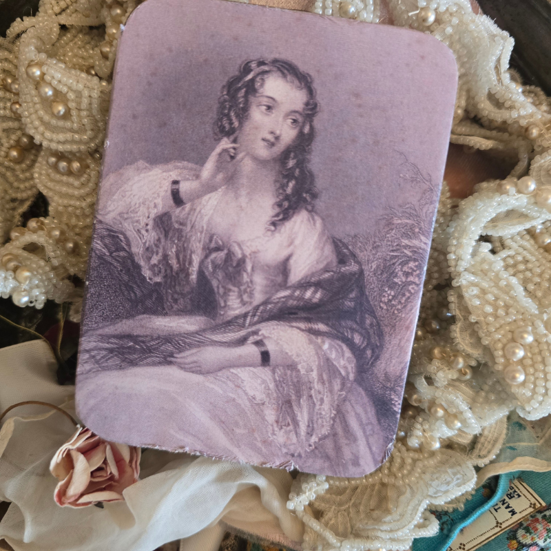 Vintage portrait print of a woman displayed among antique lace, pearl beads, faded silk flowers and collected textile fragments.