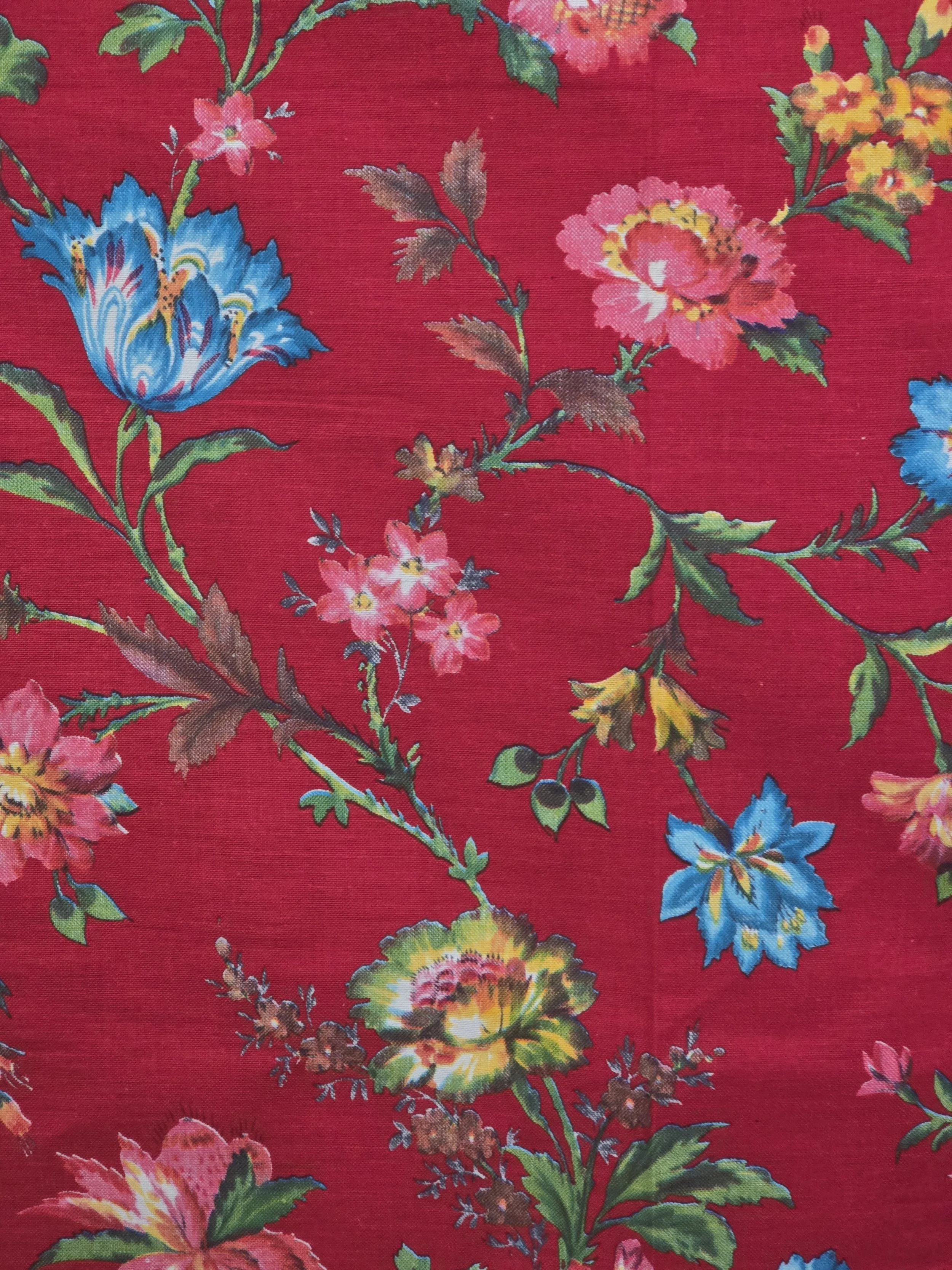 Close-up of vintage fabric showing a multicoloured flower in yellow, coral and green against a rich red background.