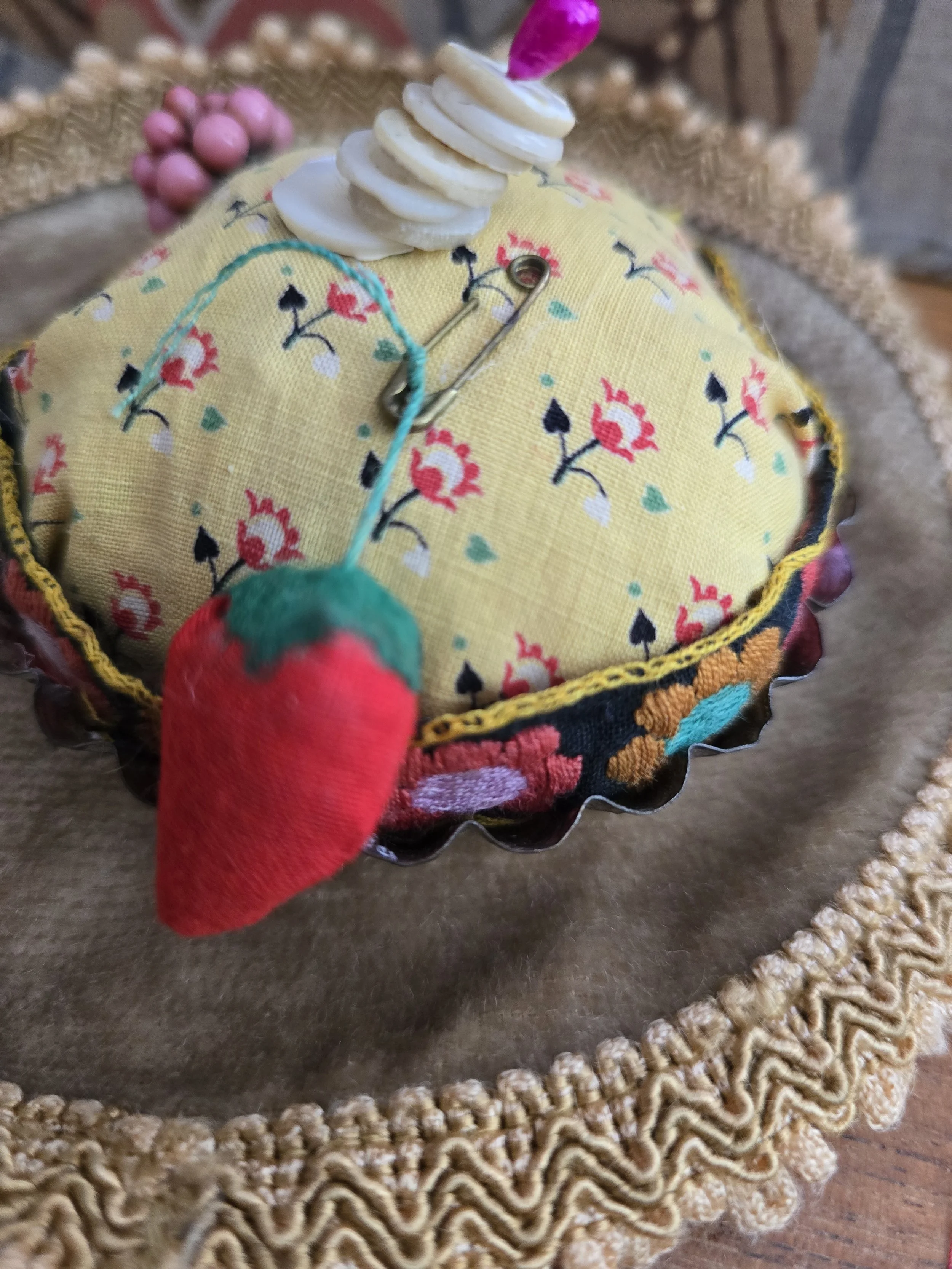 Detail of the handmade strawberry emery and aged brass safety pin attached to the pincushion.
