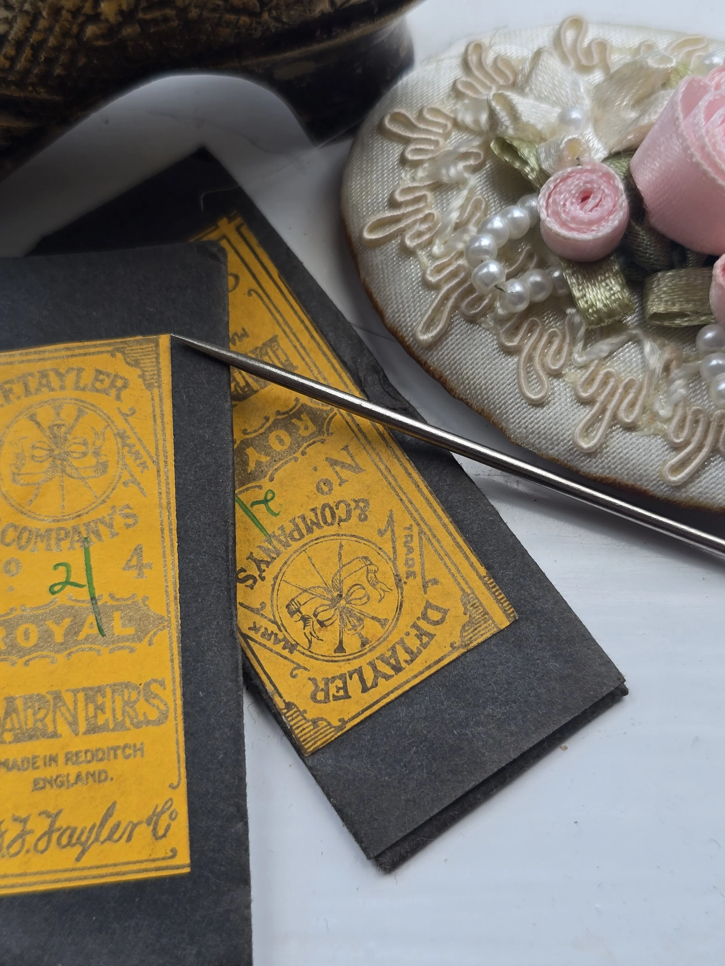 Vintage British haberdashery showing an unused D.F. Tayler Royal Darners sewing needle packet displayed with antique sewing accessories.