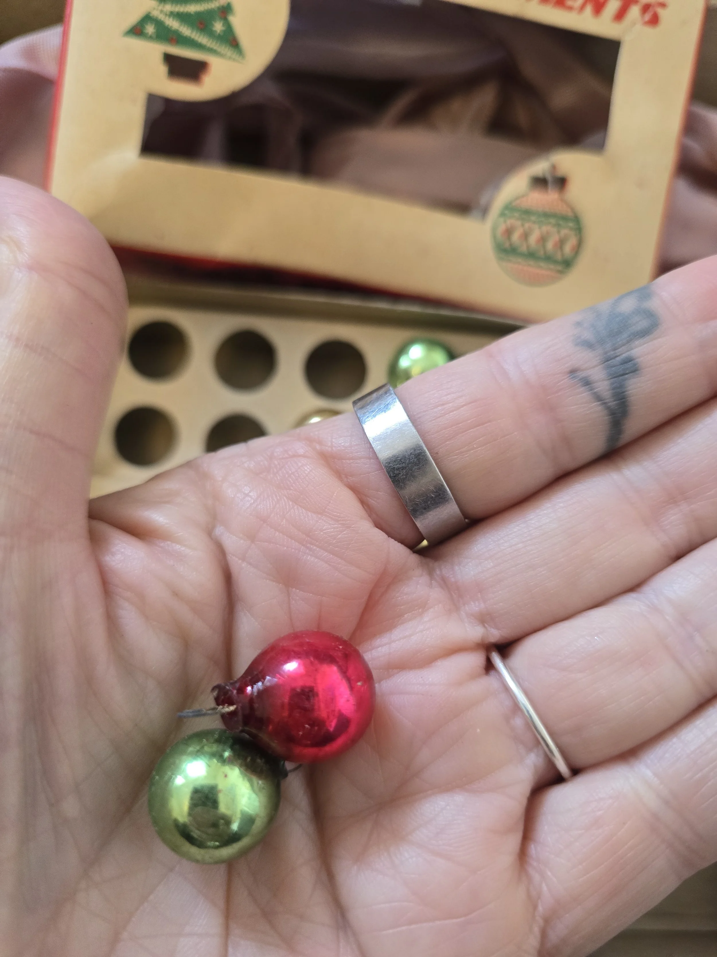 Two tiny vintage glass Christmas baubles in red and green, shown in a hand to illustrate their 15 mm size.