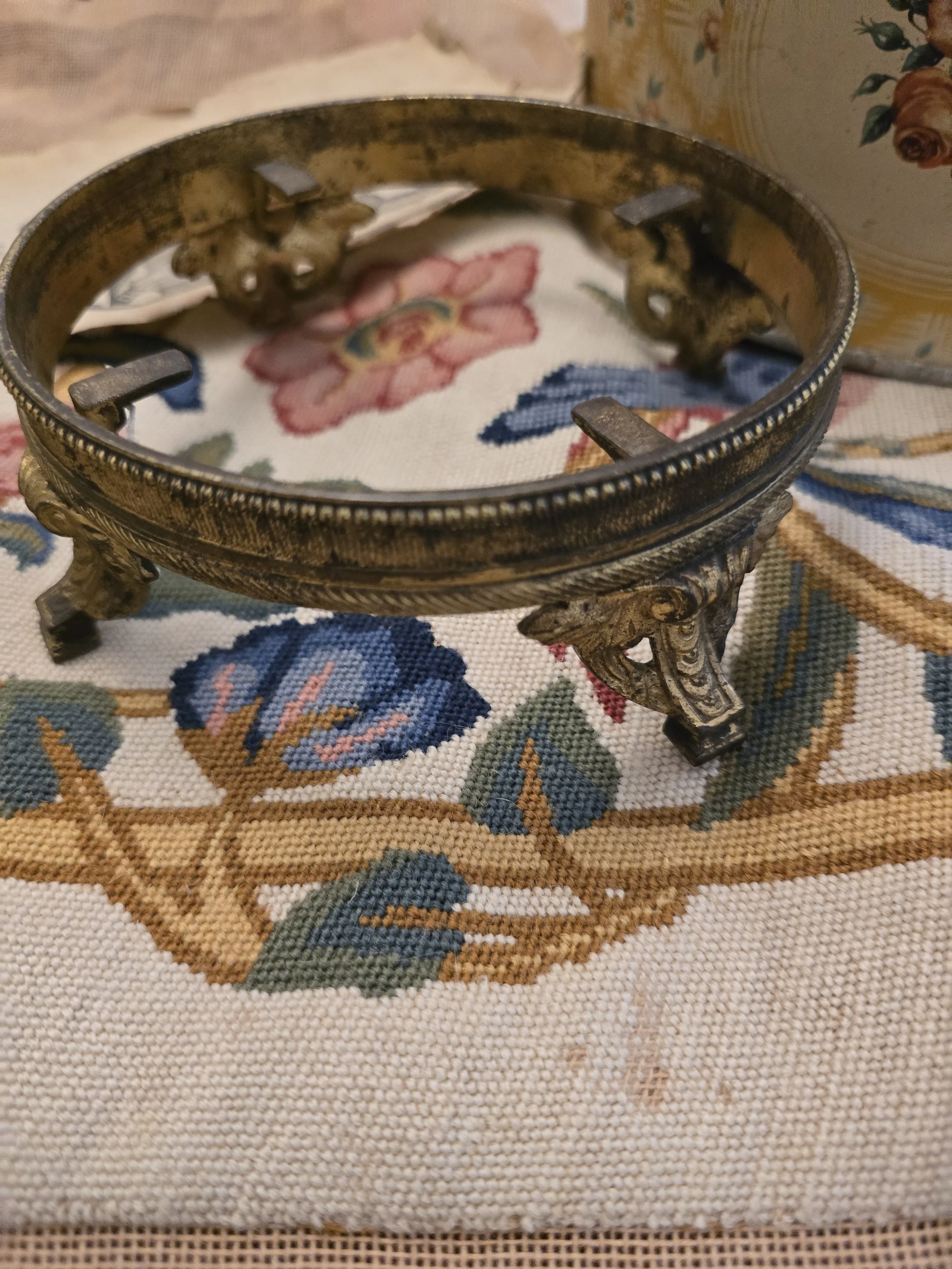 Vintage circular gilt metal bowl stand with ornate decorative feet and aged gold finish.