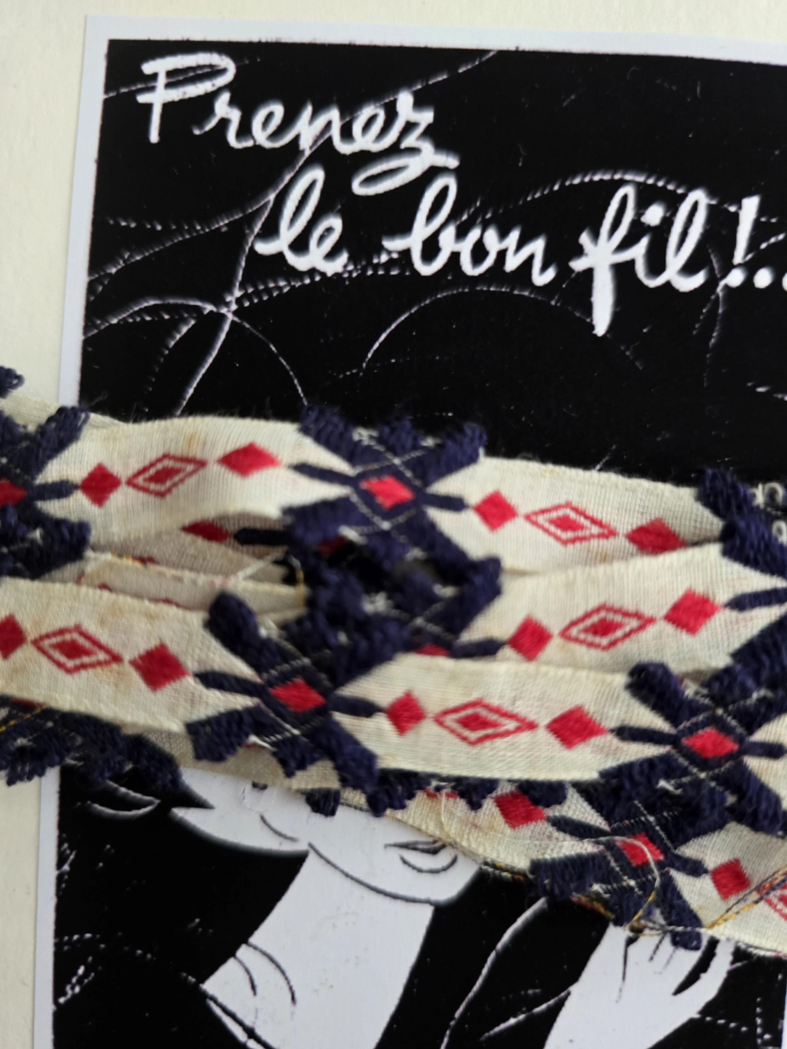 Close-up of narrow vintage French haberdashery trim with red diamond motifs and raised navy woven decoration.