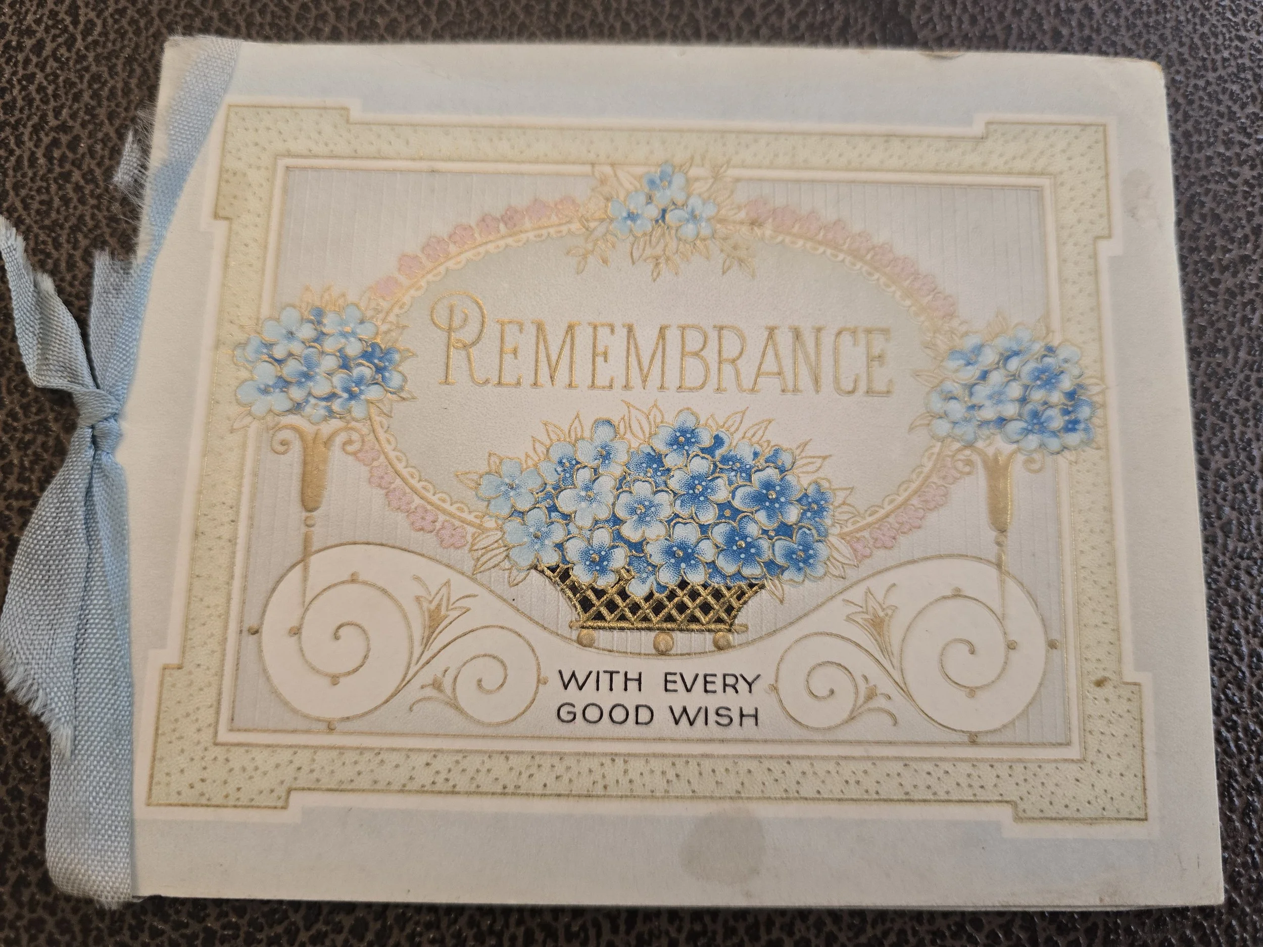 Front of a 1935 vintage Christmas remembrance card with blue forget-me-not flowers, gold lettering and pale blue ribbon.