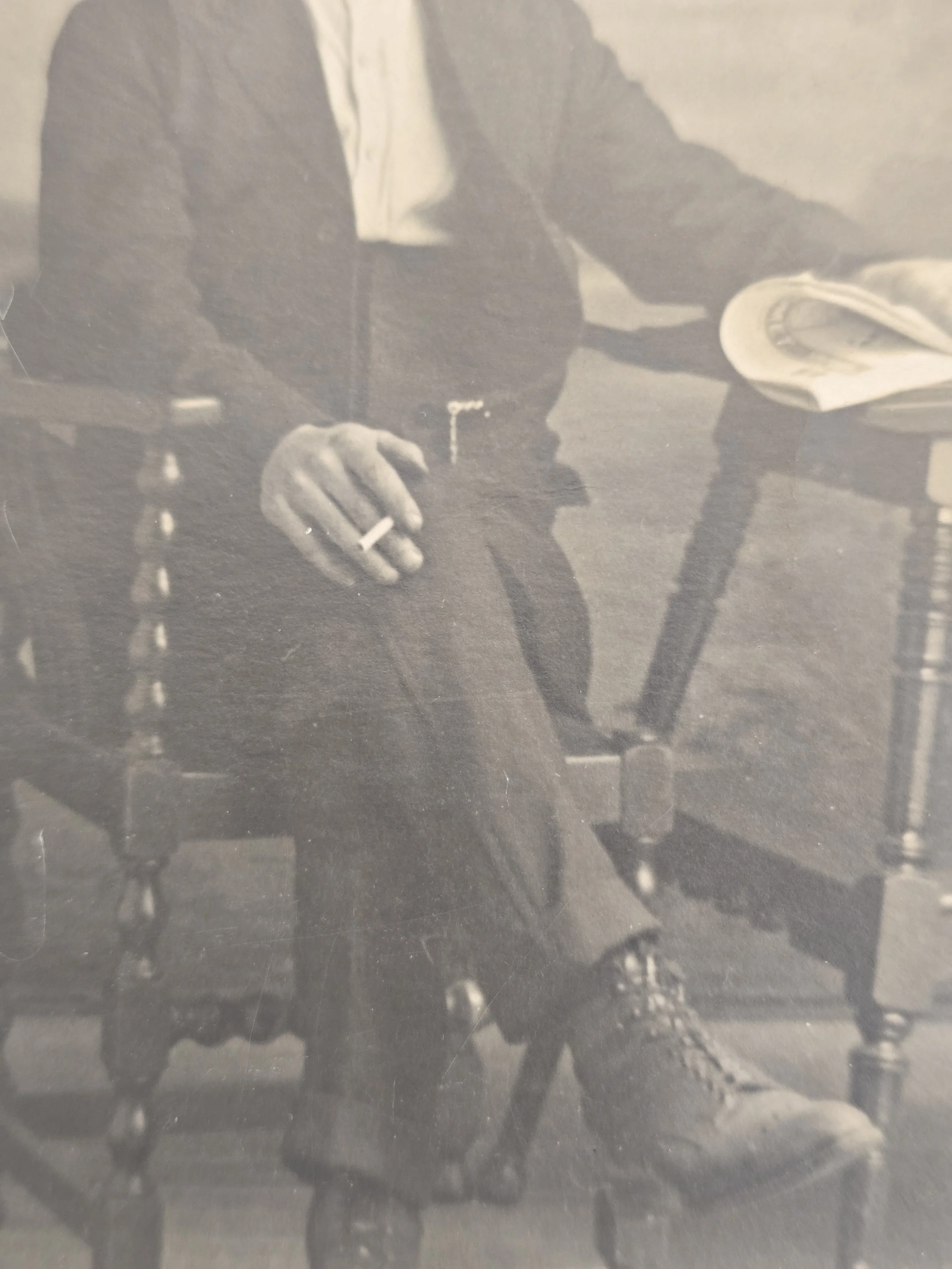 Detail of an early 20th-century male studio portrait showing high-waisted trousers, cigarette and lace-up boots.