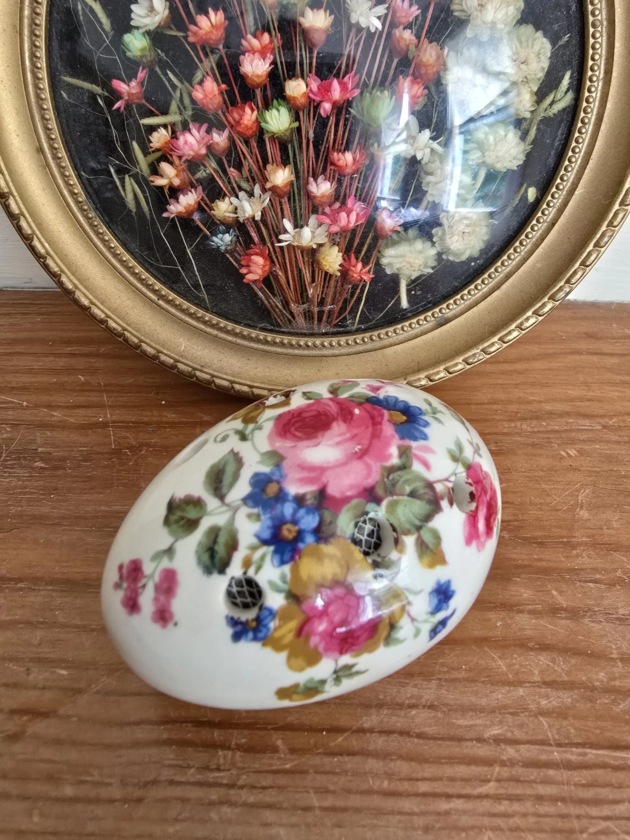 Close-up of vintage ceramic pomander with floral pattern and mesh holes, styled against dried flower frame