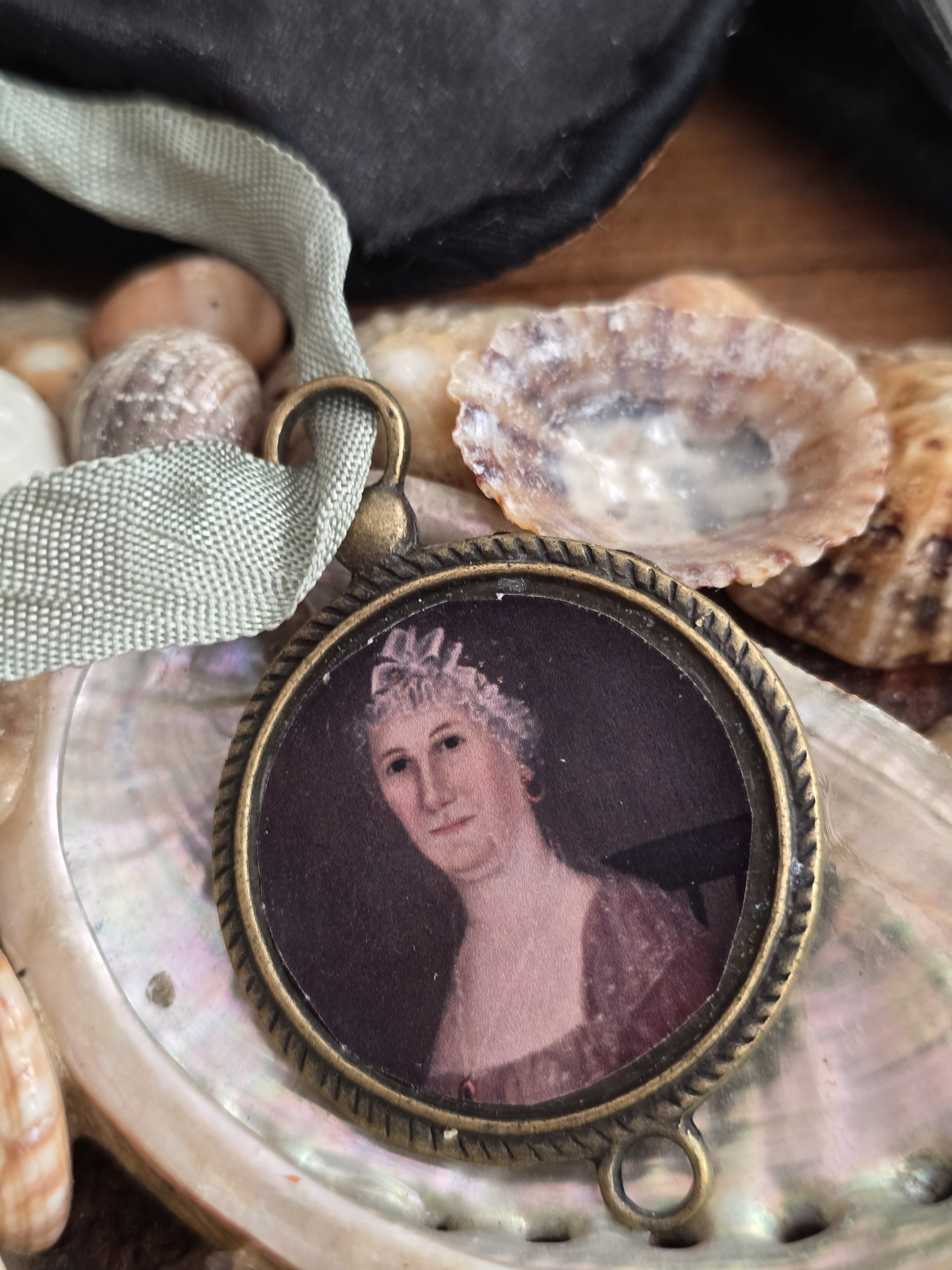 Studio Made decorative portrait hanging with vintage sage green ribbon, displayed amongst a collection of old seashells.