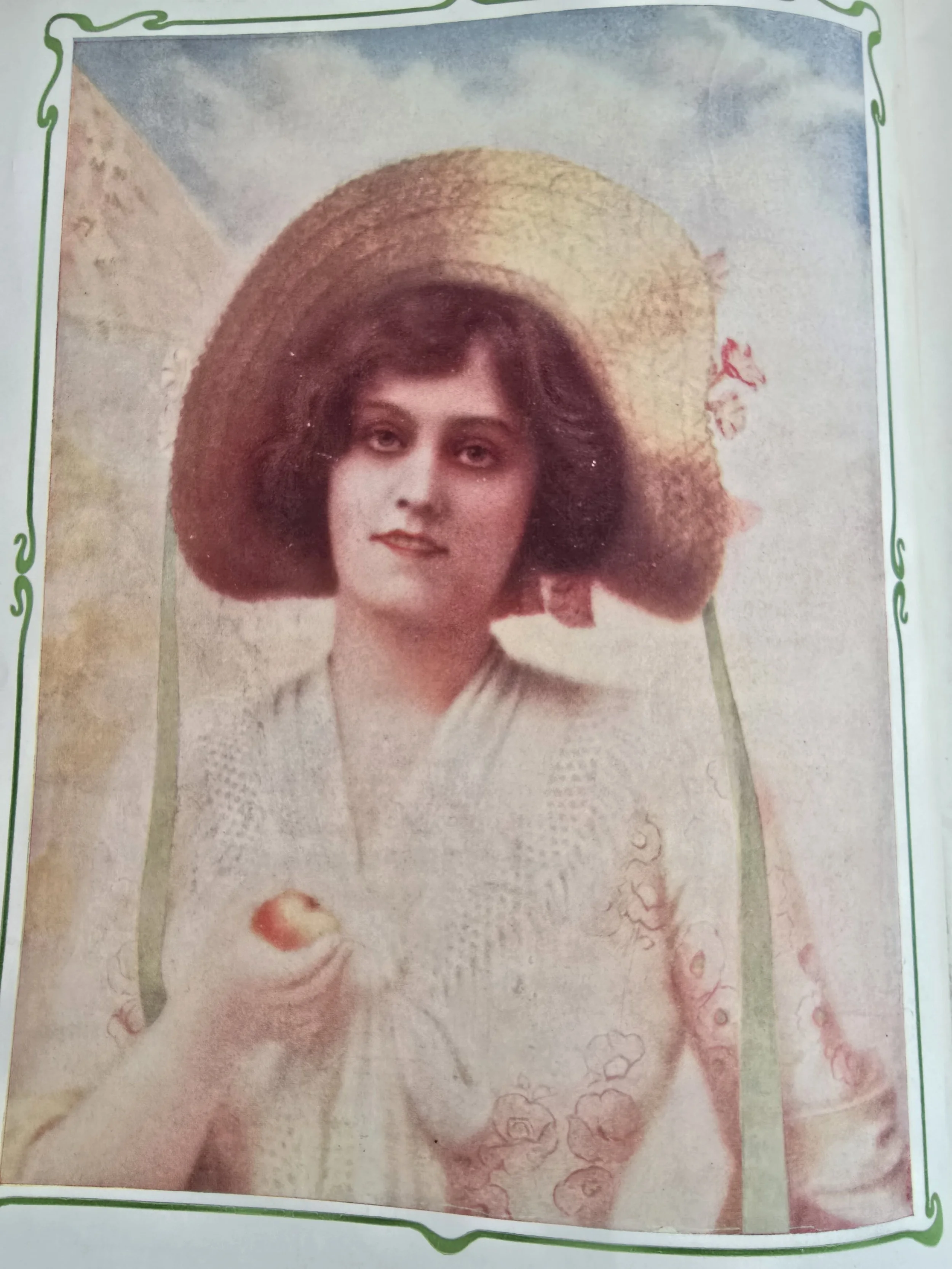 Hand-tinted portrait from The Play Pictorial featuring a woman with a straw hat holding an apple