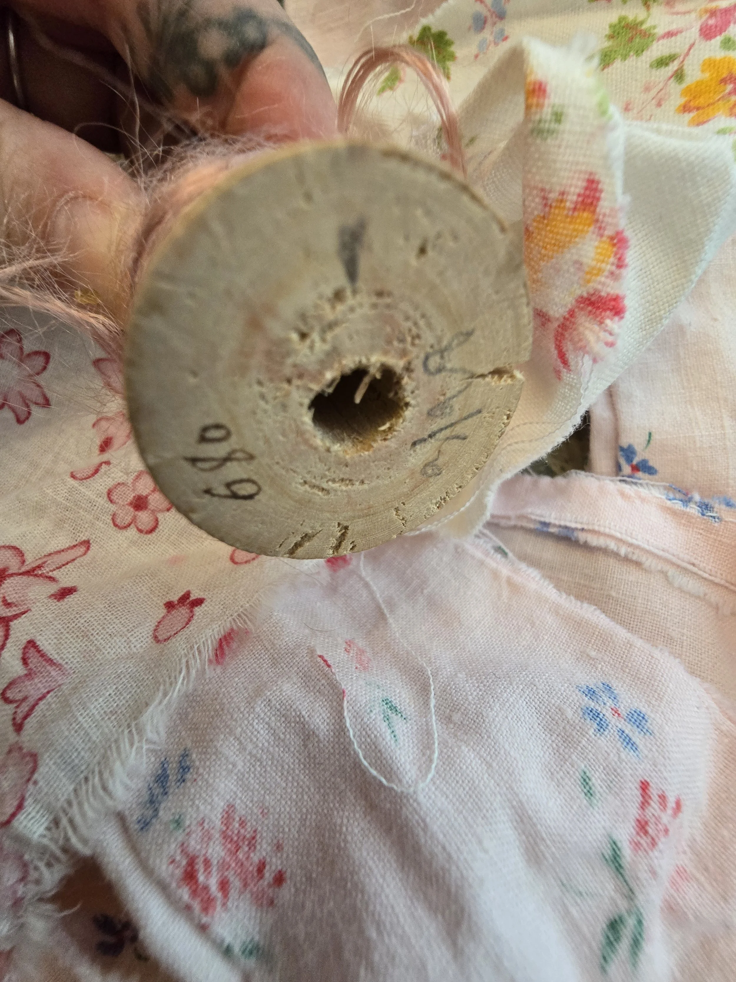 Close-up of antique pink thread on original wooden sewing spool with handwritten markings.