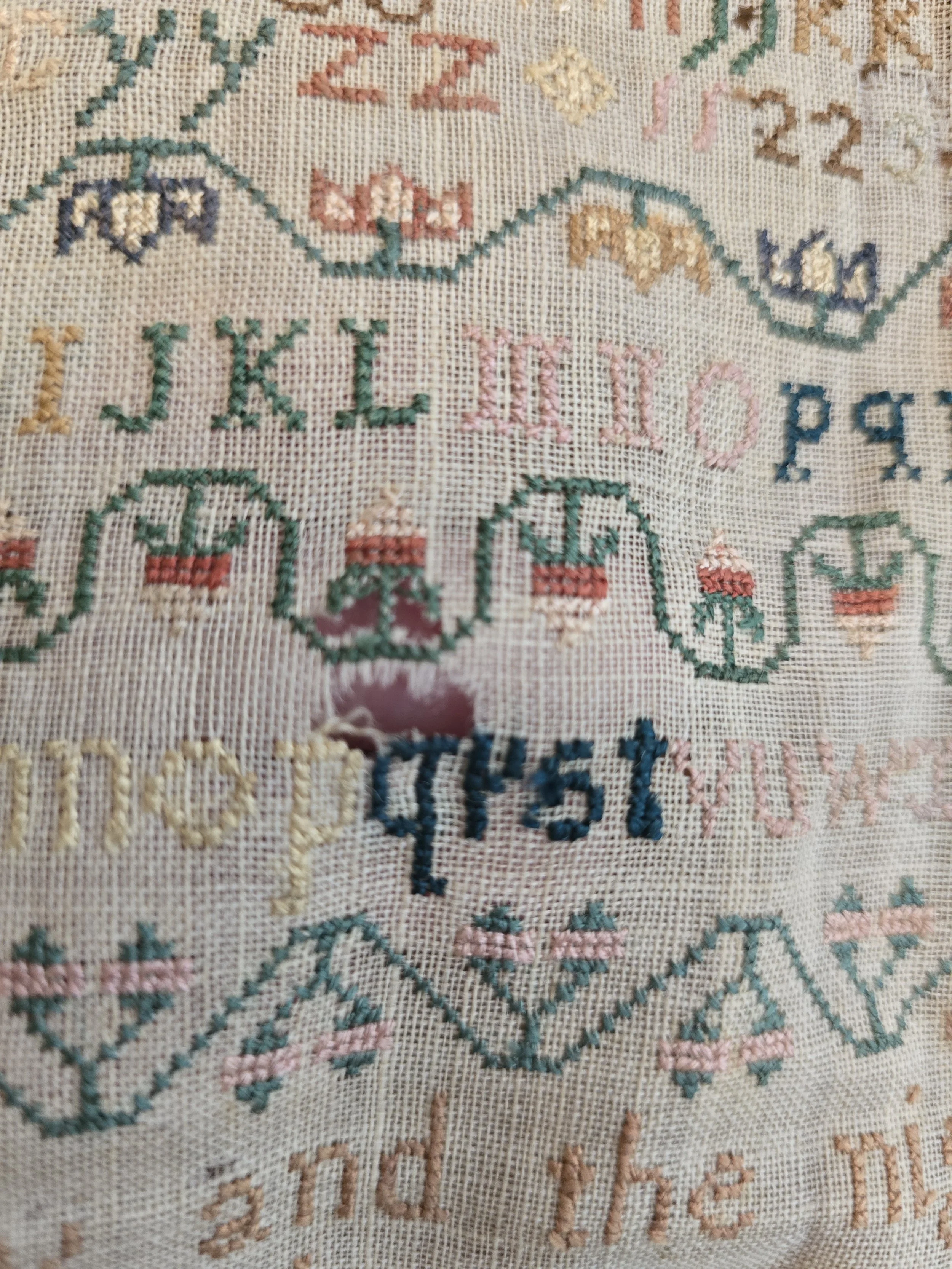 Early nineteenth century linen sampler featuring rows of stitched letters, numbers and ornamental needlework.
