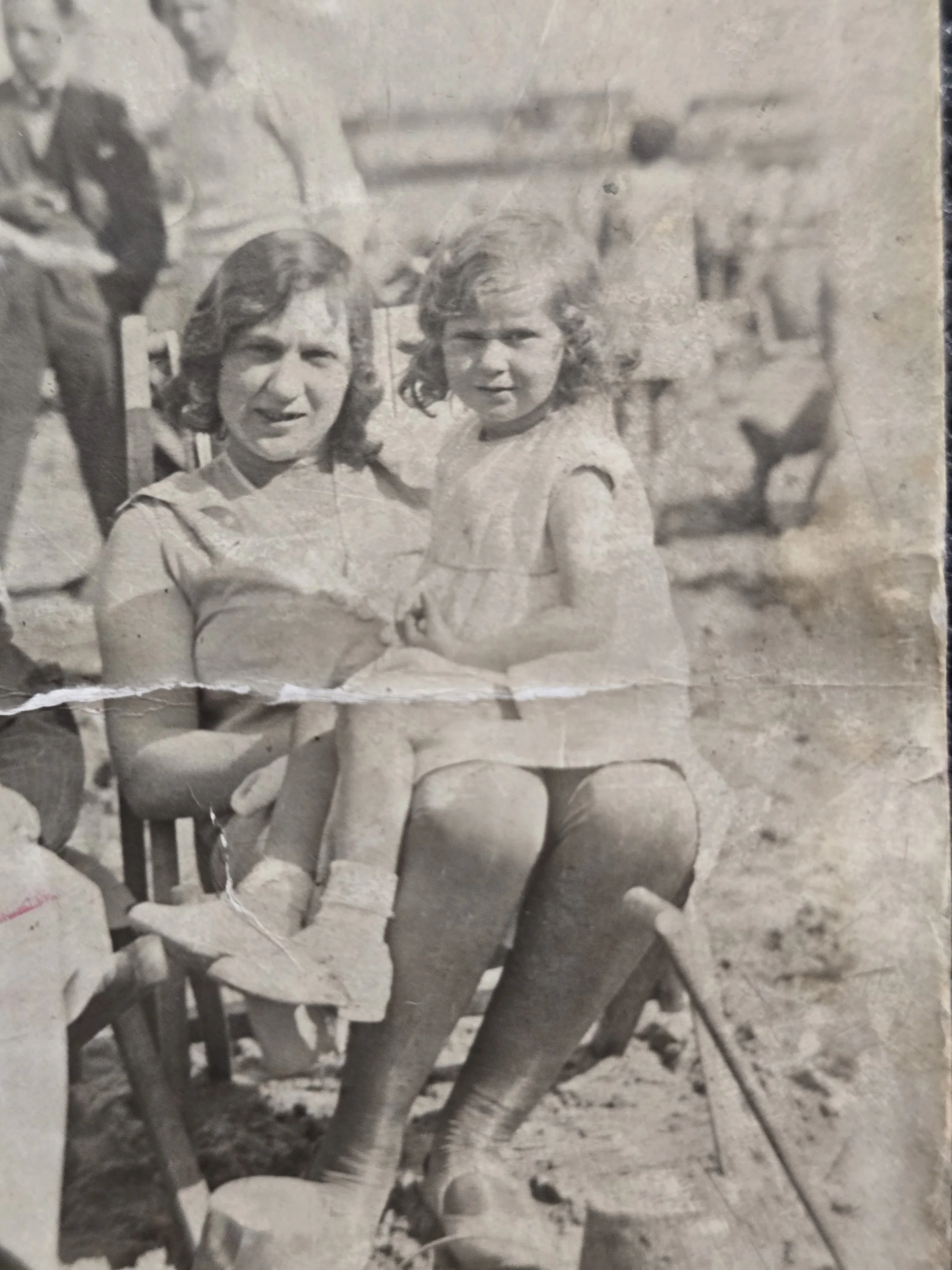 Woman holding a young girl beside a bucket and spade in an original 1930s seaside family photograph.
