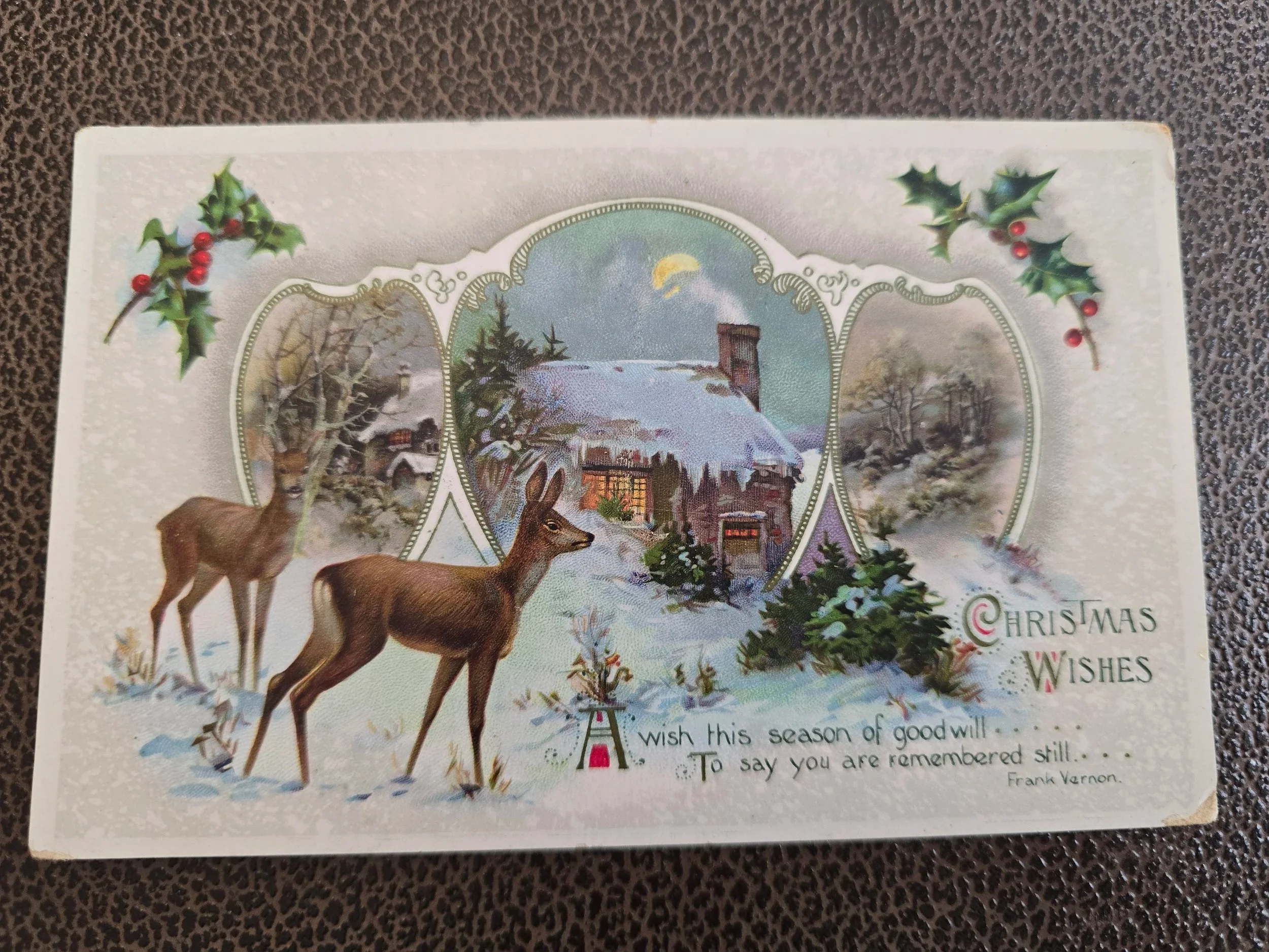 Front of a 1914 Christmas postcard depicting two deer in a snowy landscape, a warmly lit cottage, winter scenes and holly.