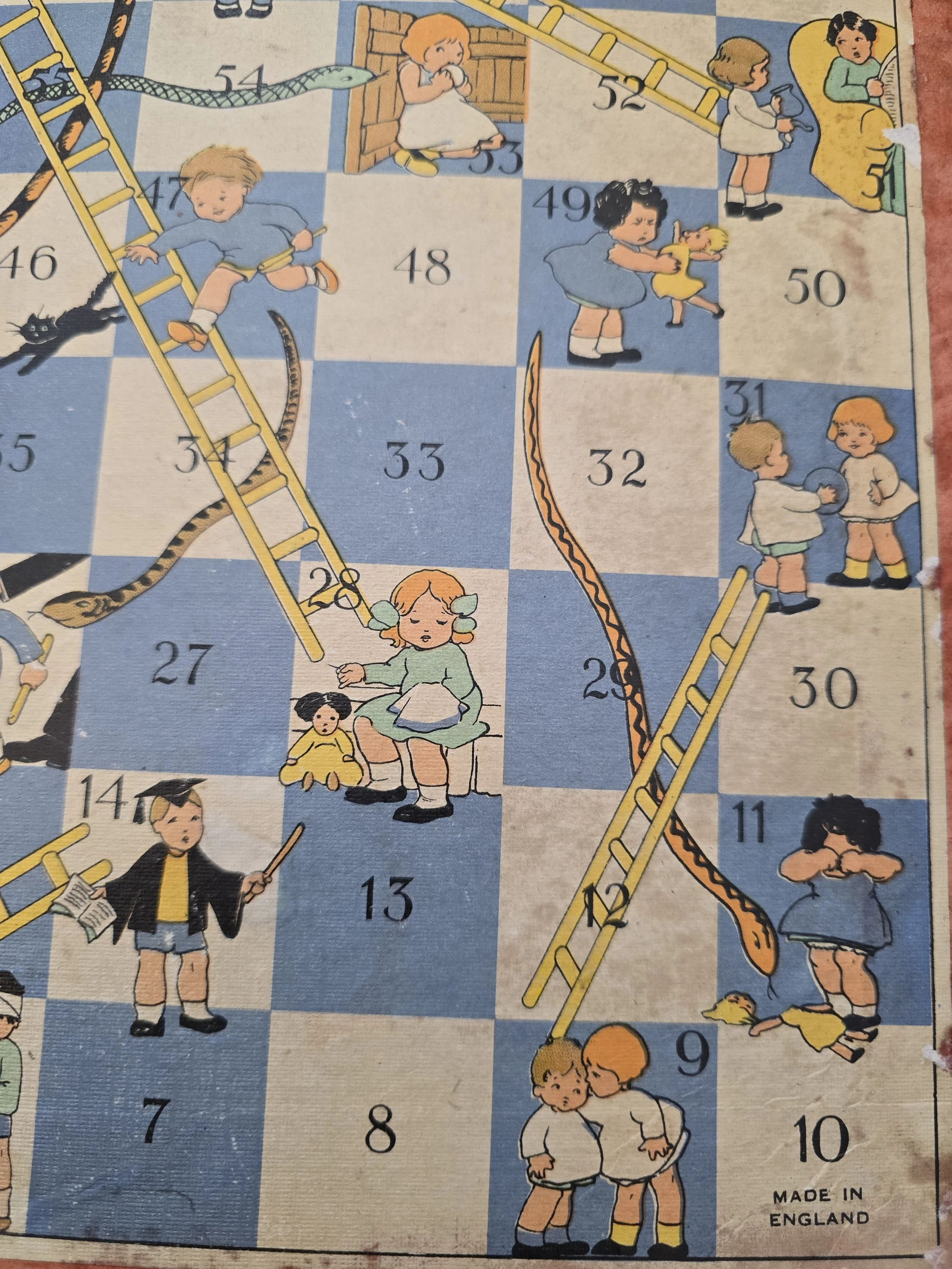 Worn vintage Snakes and Ladders board showing children, dolls and snakes