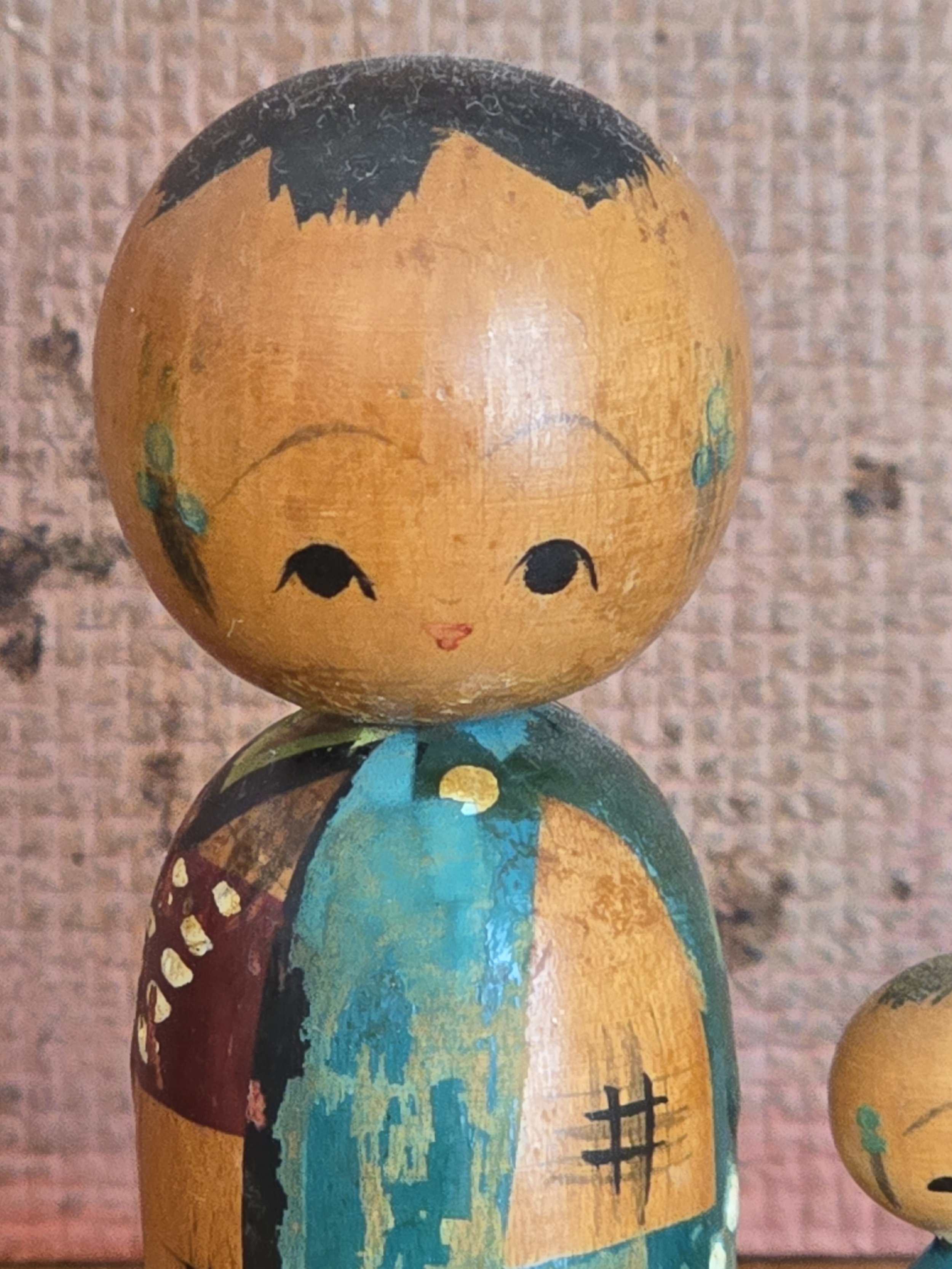Close-up of the largest vintage kokeshi doll with turquoise robe and traditional painted facial features.