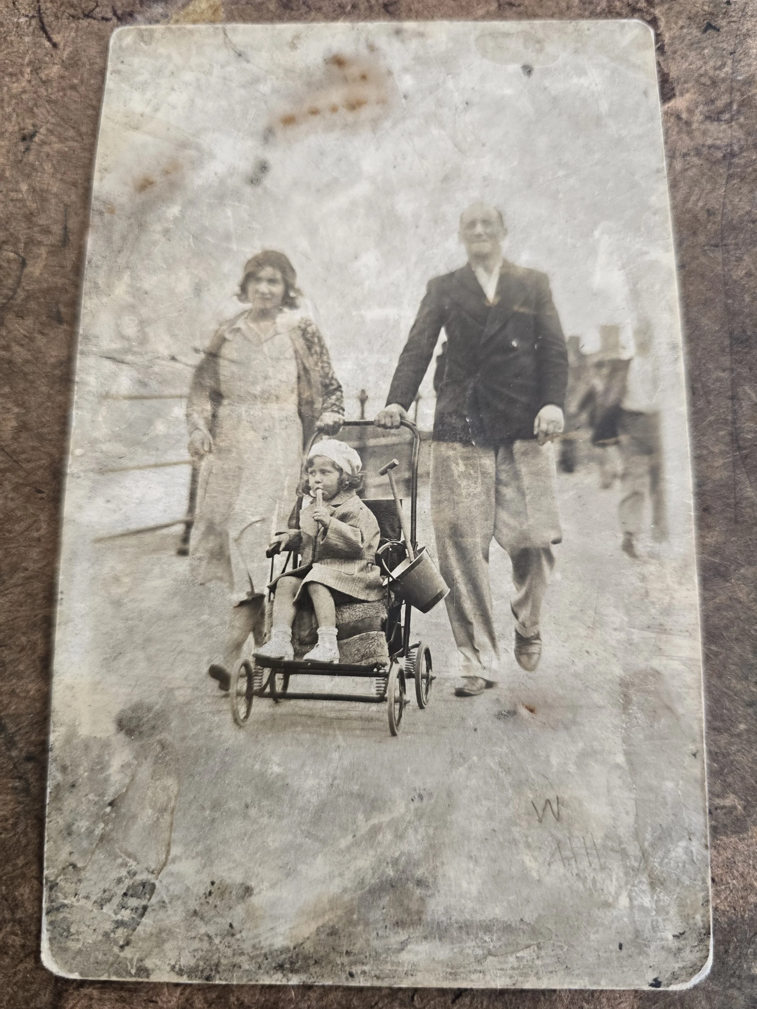 Vintage photographic postcard showing a family walking along a seaside promenade.