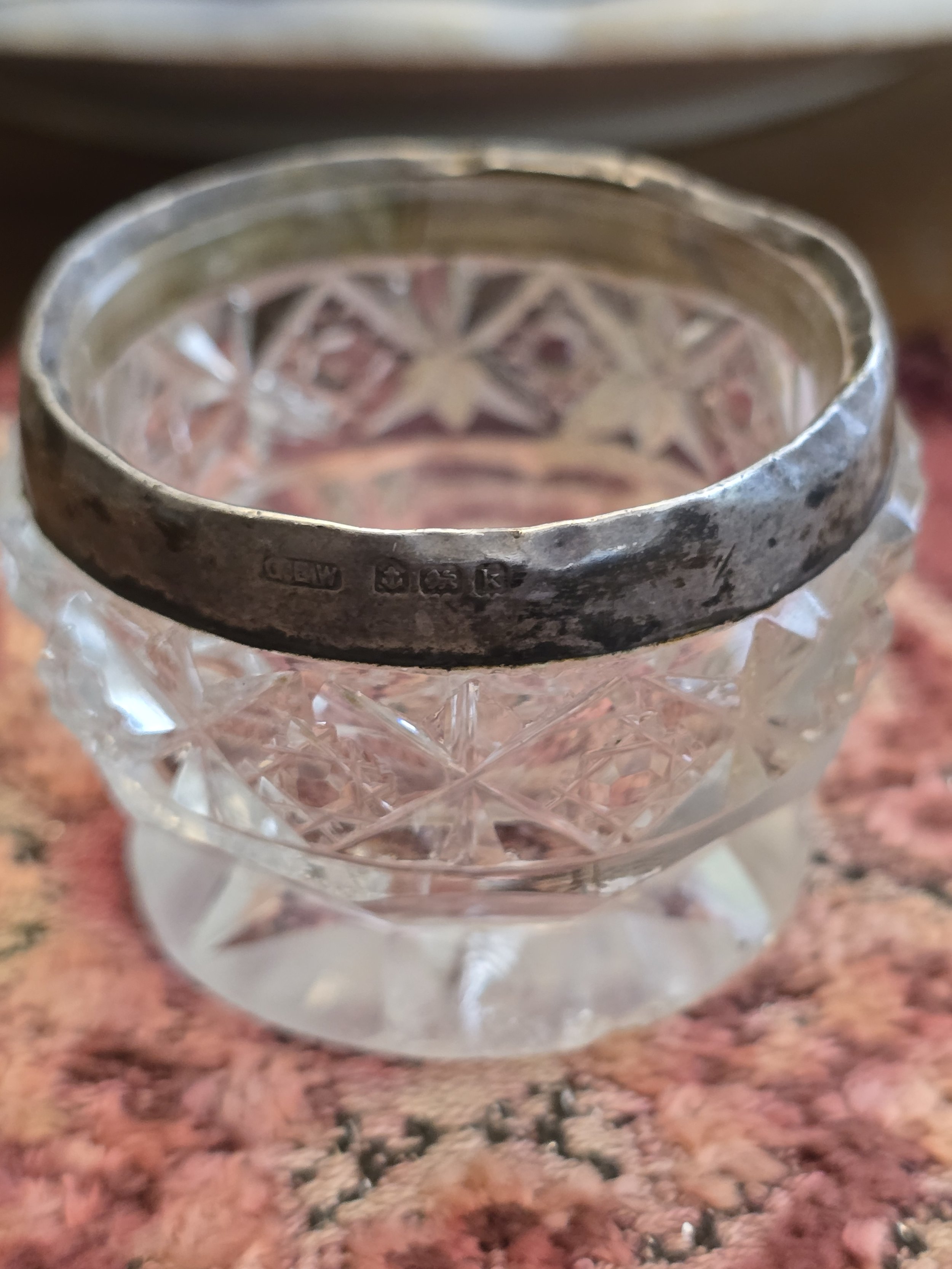 Small antique English salt cellar with geometric cut glass body and tarnished silver rim.