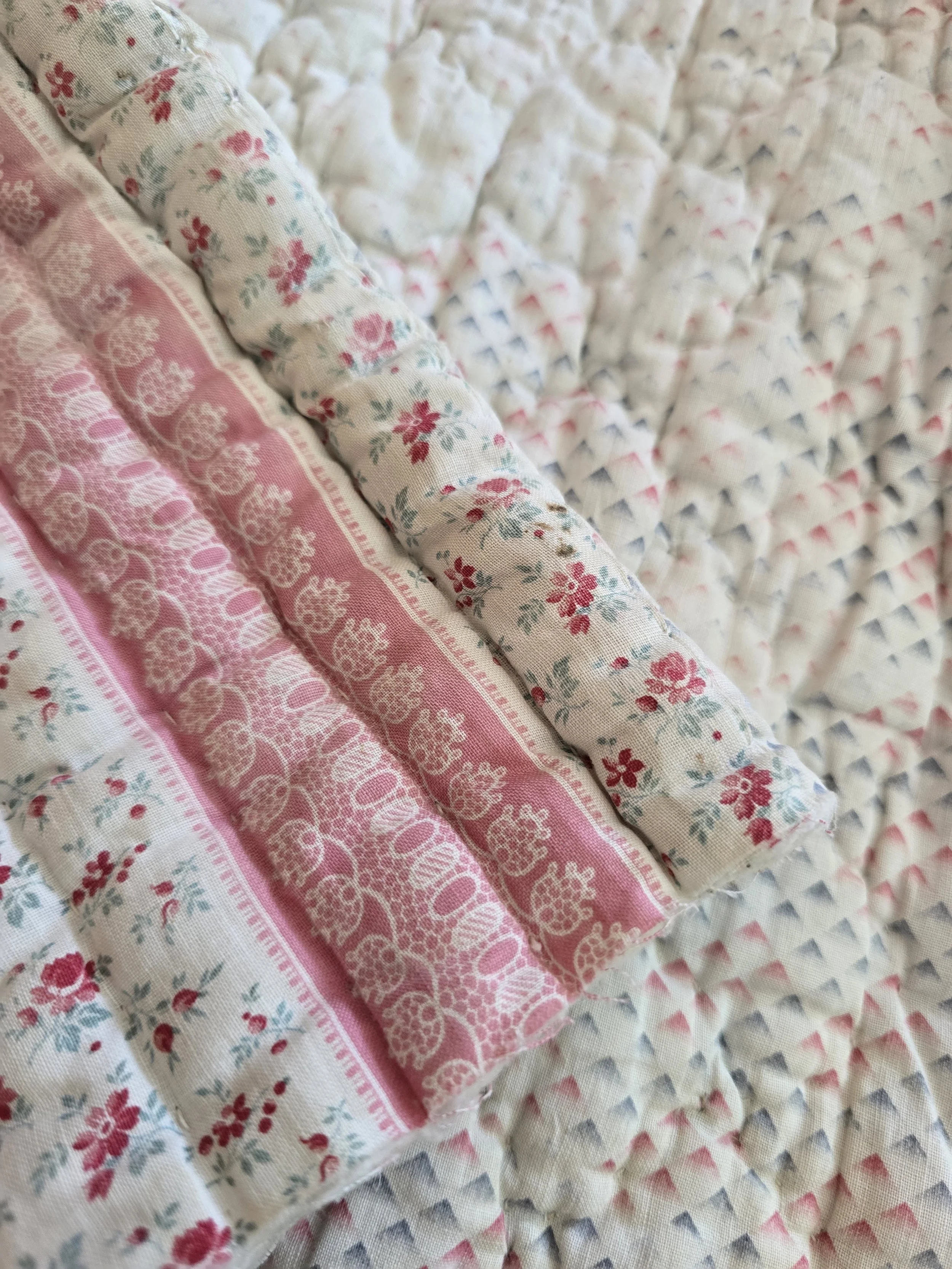 Close-up of vintage French floral quilted fabric with rosebud motif and pink decorative bands.