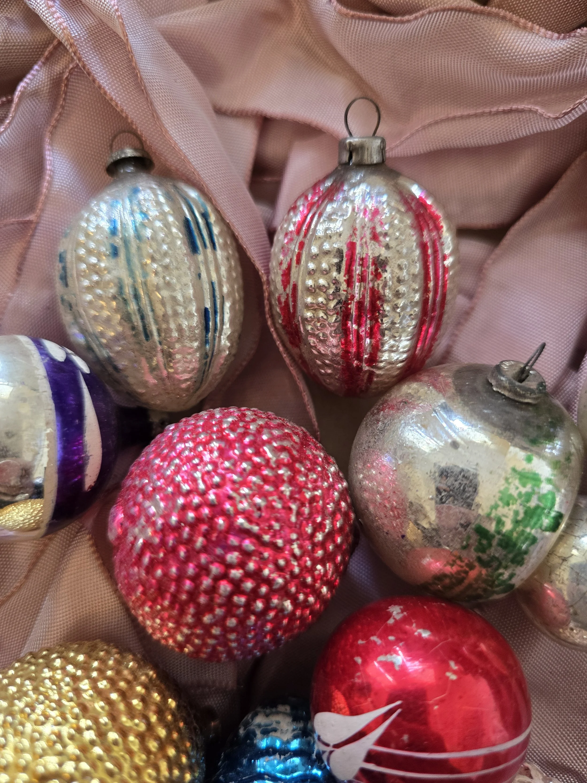 Assorted vintage Christmas ornaments including red and gold textured glass baubles and a blue pinecone decoration.