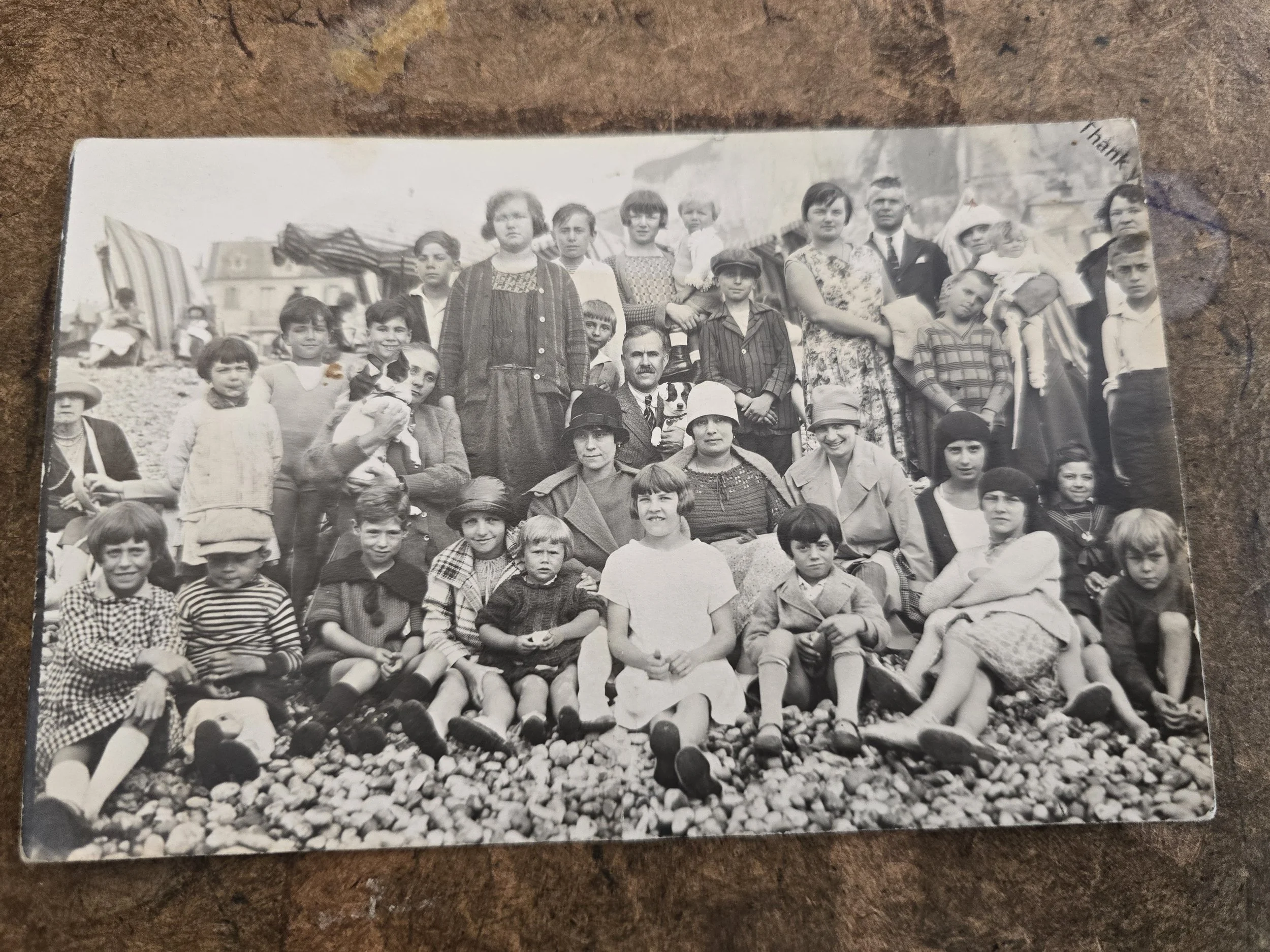 Original French photographic postcard showing a large family group gathered on a pebble beach.