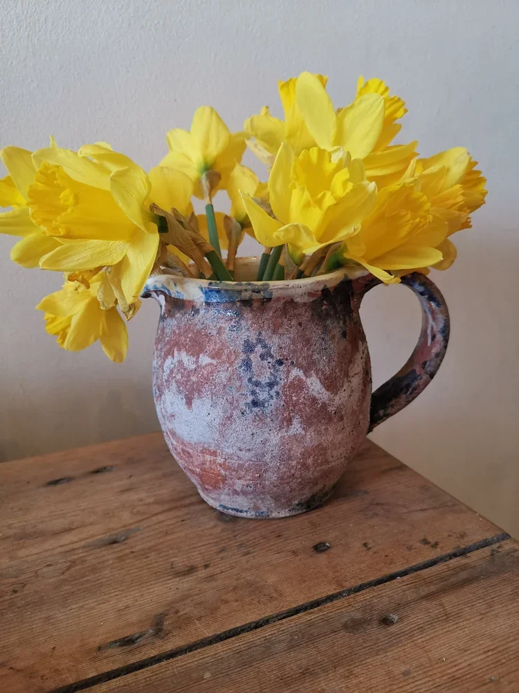 Top view of antique French terracotta pitcher filled with bright yellow daffodils
