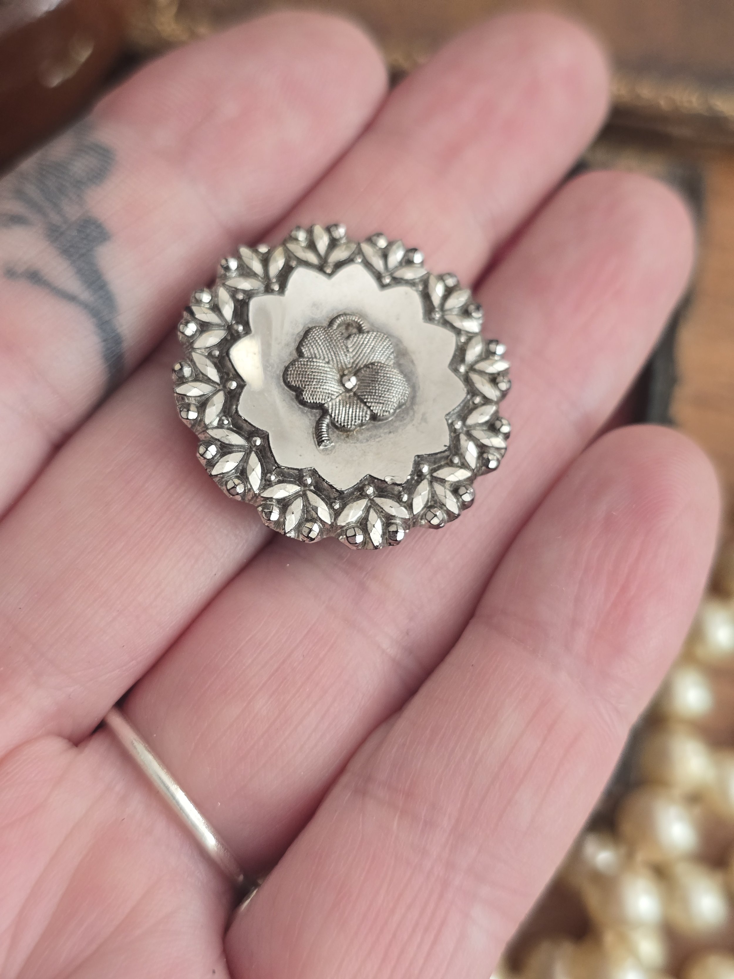 Antique Victorian pressed steel button with engraved shamrock centre resting on a hand.