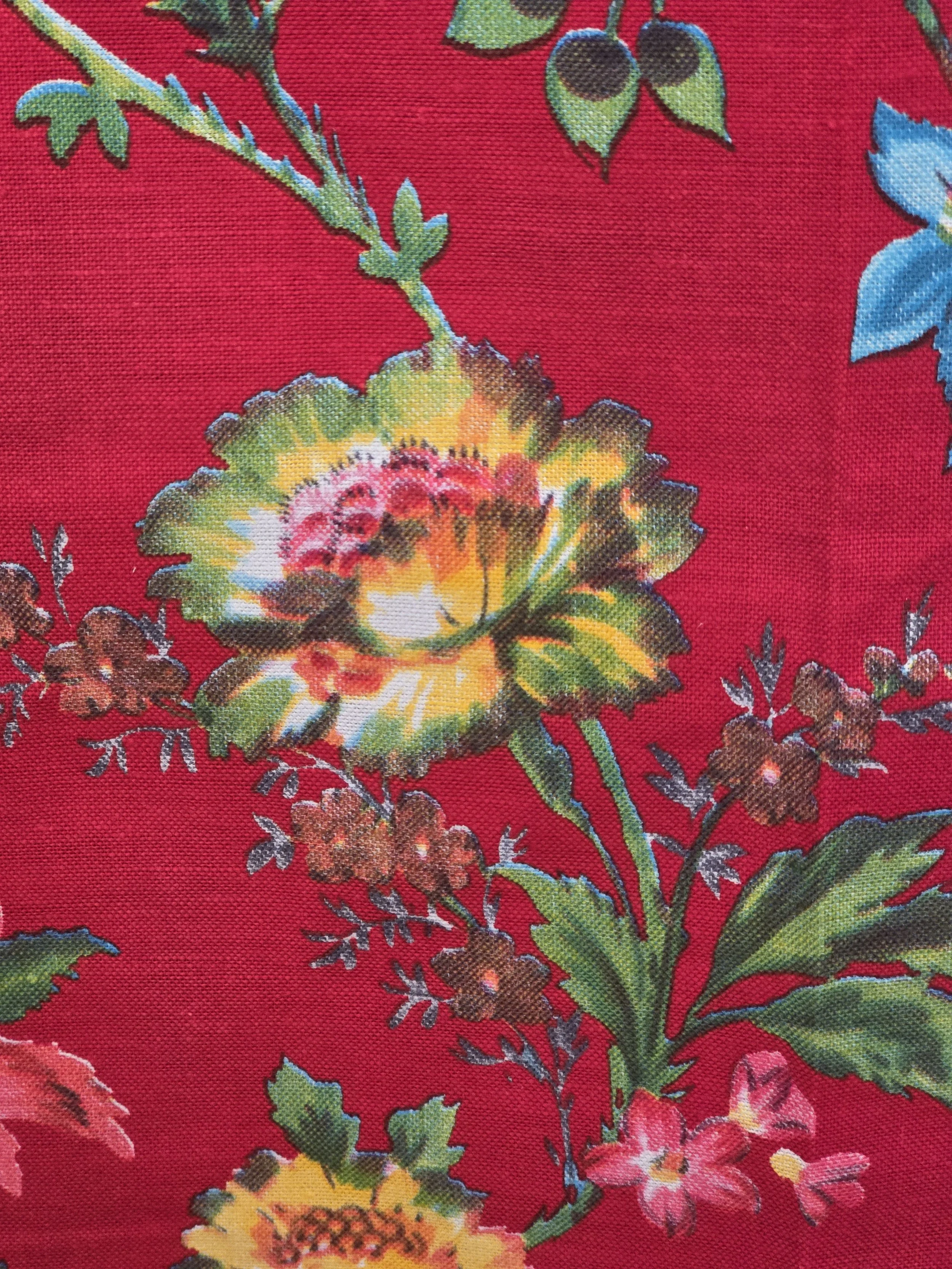 Detail of vintage red floral fabric with turquoise blue flowers, pink blossoms and trailing green foliage.