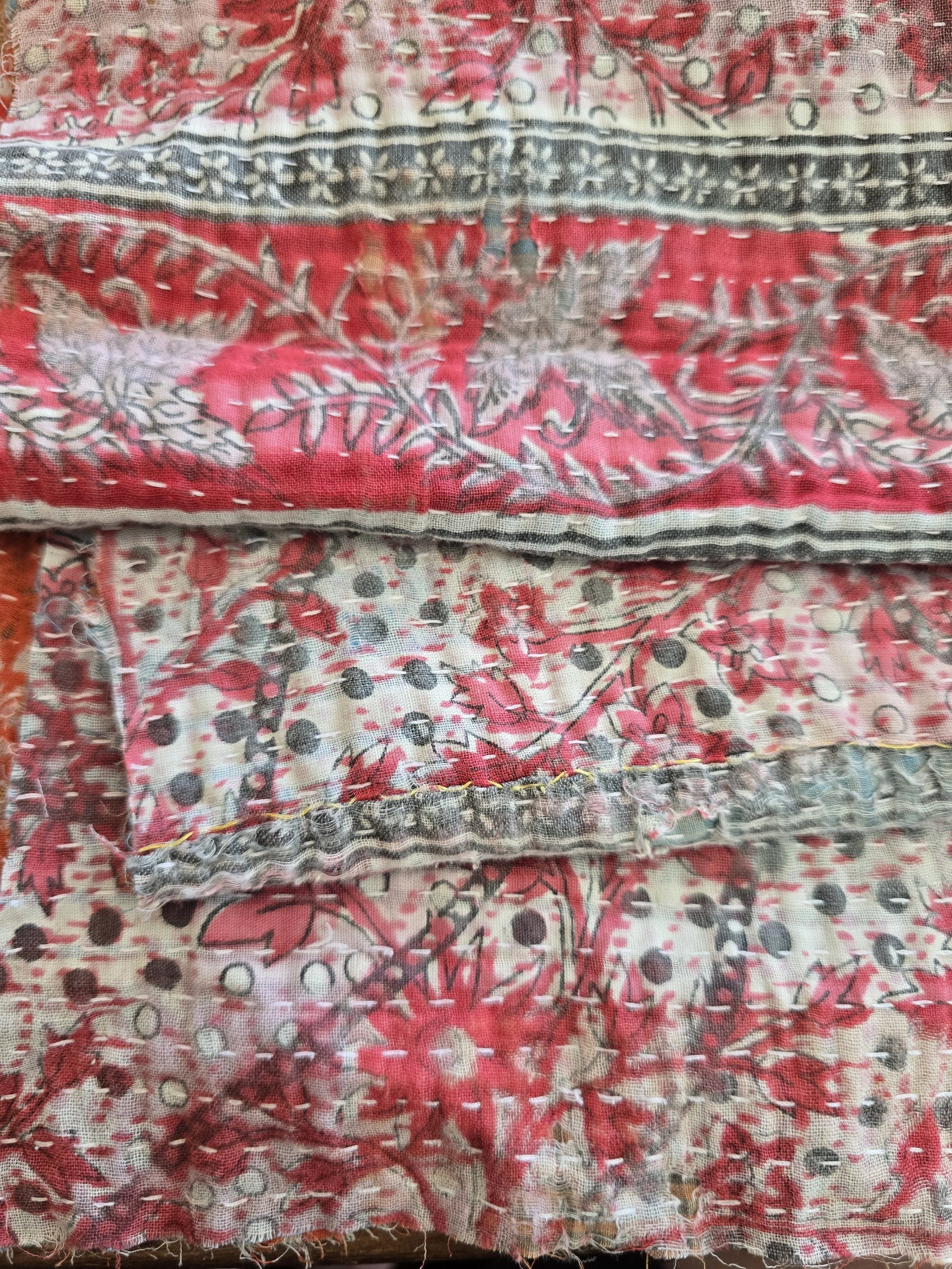 Vintage kantha textile fragment with hand stitching and layered cotton fabrics in red, cream and blue tones.