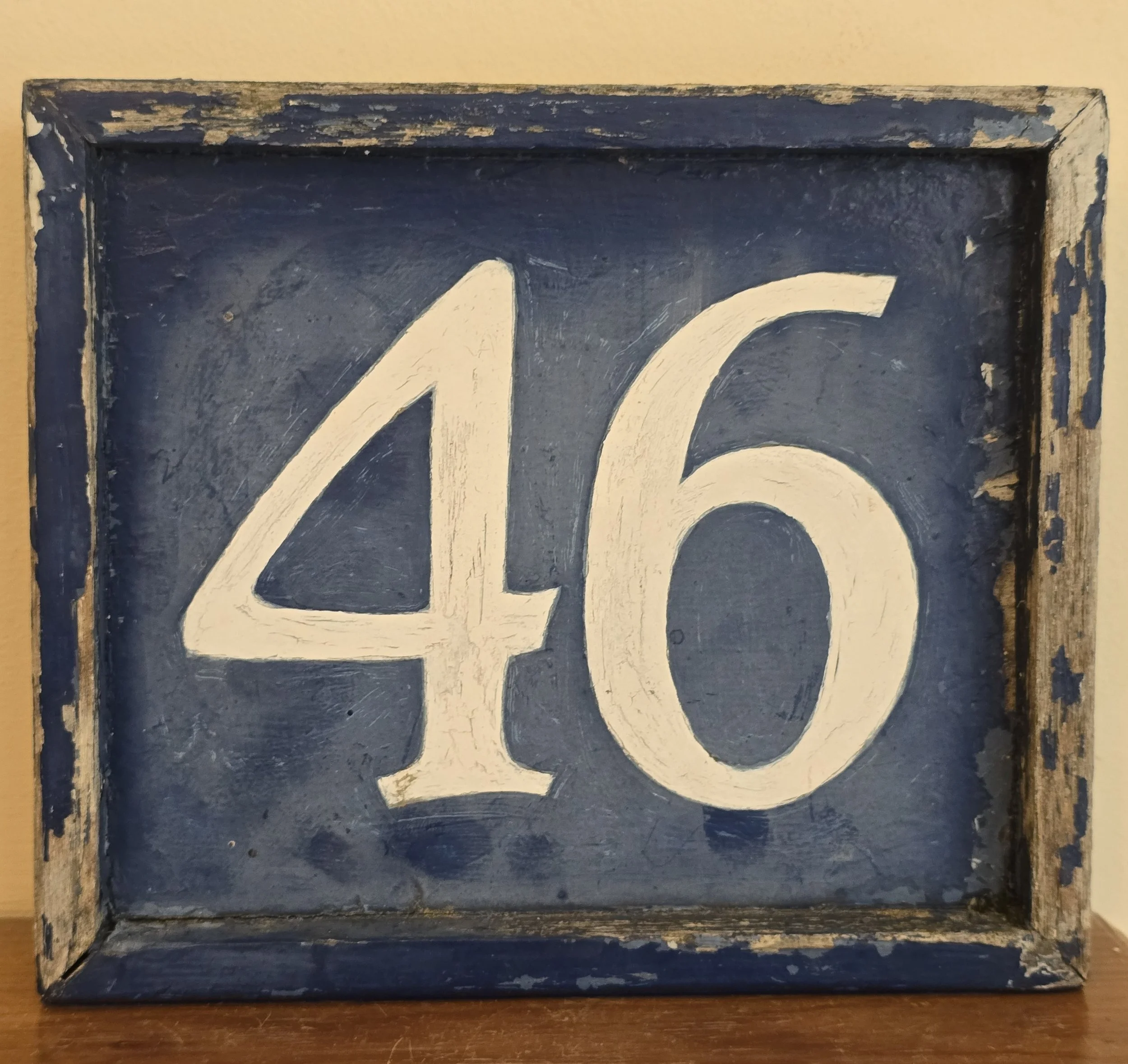 Vintage hand-painted wooden number sign displaying the number 46 on a blue background.