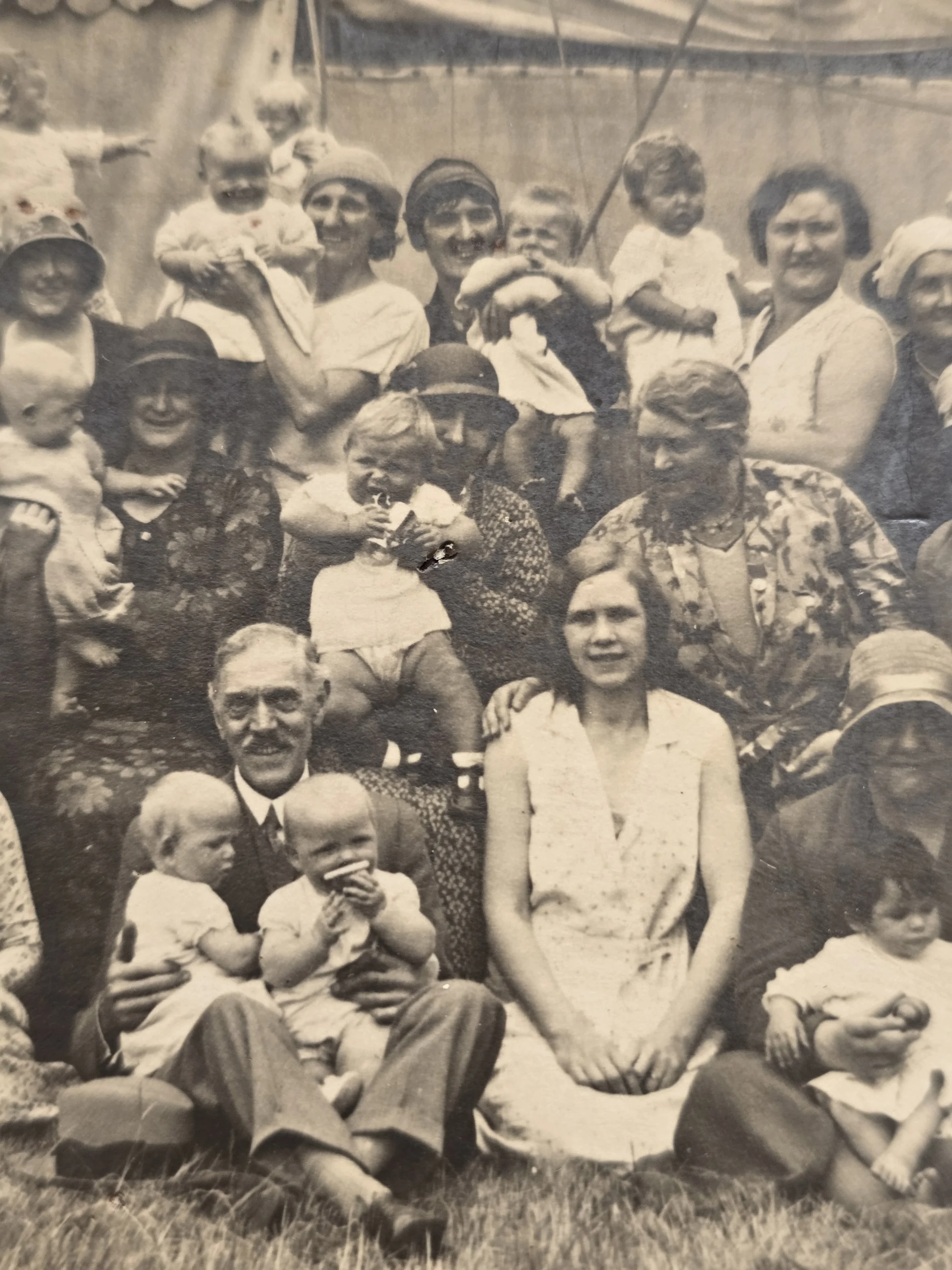 Detail of 1930s group photograph showing women holding babies beneath a large canvas tent.