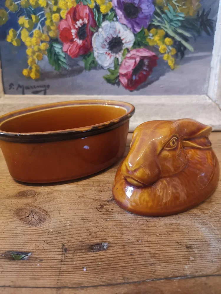 Open French terrine with rabbit lid placed beside caramel-brown base
