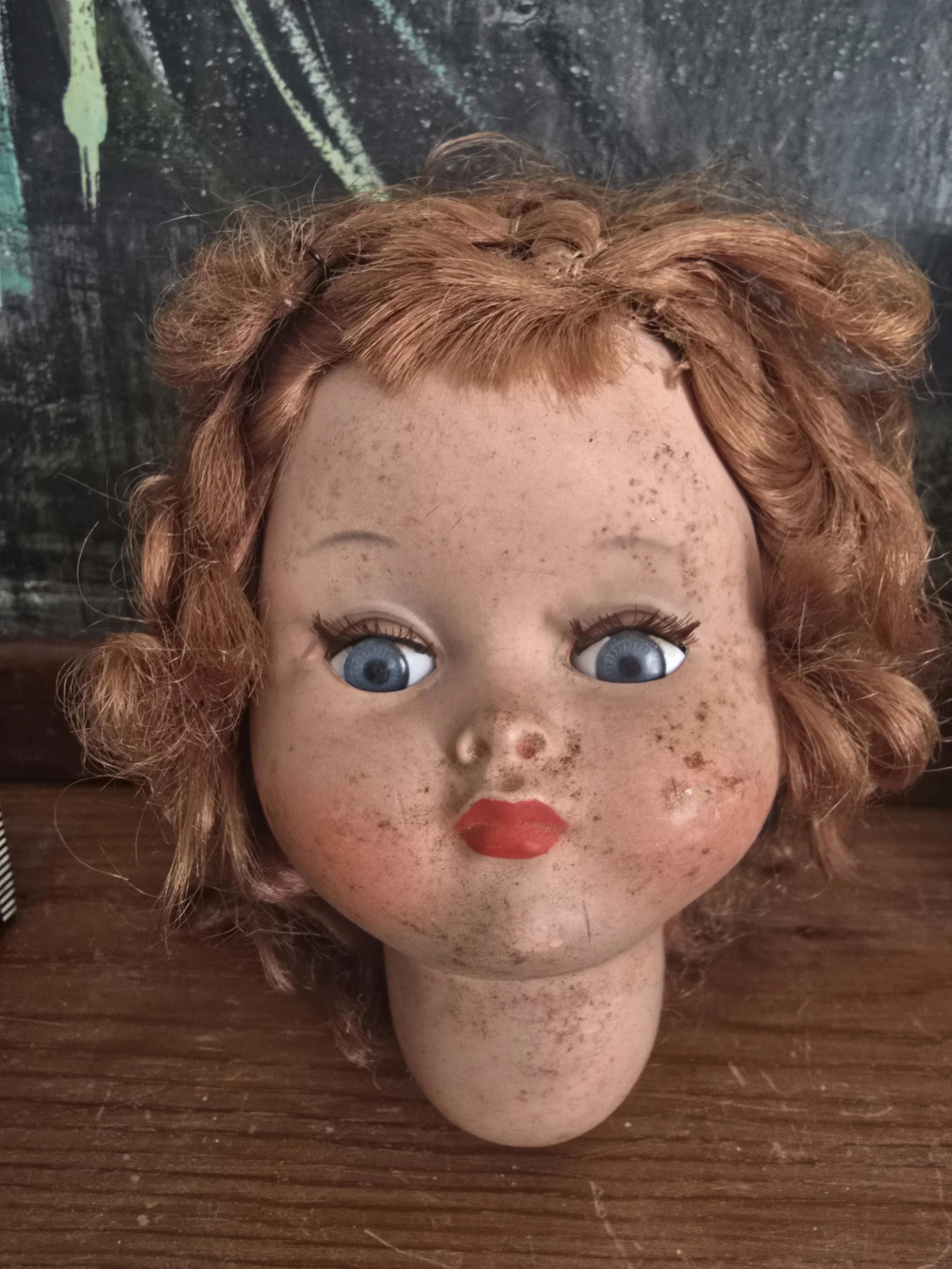 Front view of aged French doll head with blue eyes, painted lashes and visible timeworn patina