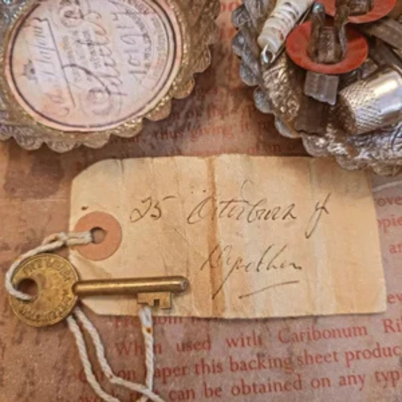 Antique brass key with handwritten vintage luggage tag, layered over aged French papers, labels and textile fragments.