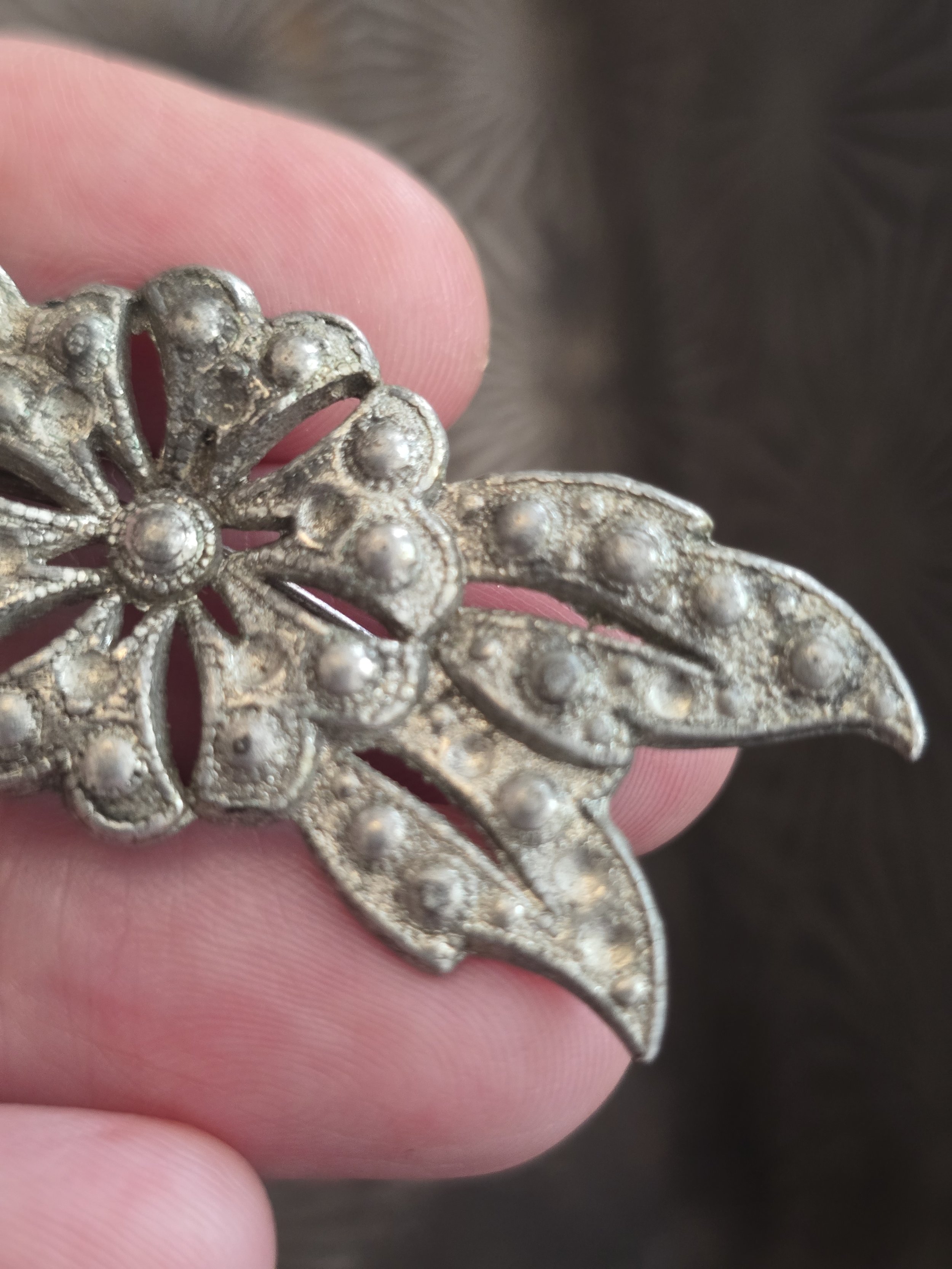 Detailed close-up of vintage silver-tone floral brooch with textured surface and decorative leaf motifs.