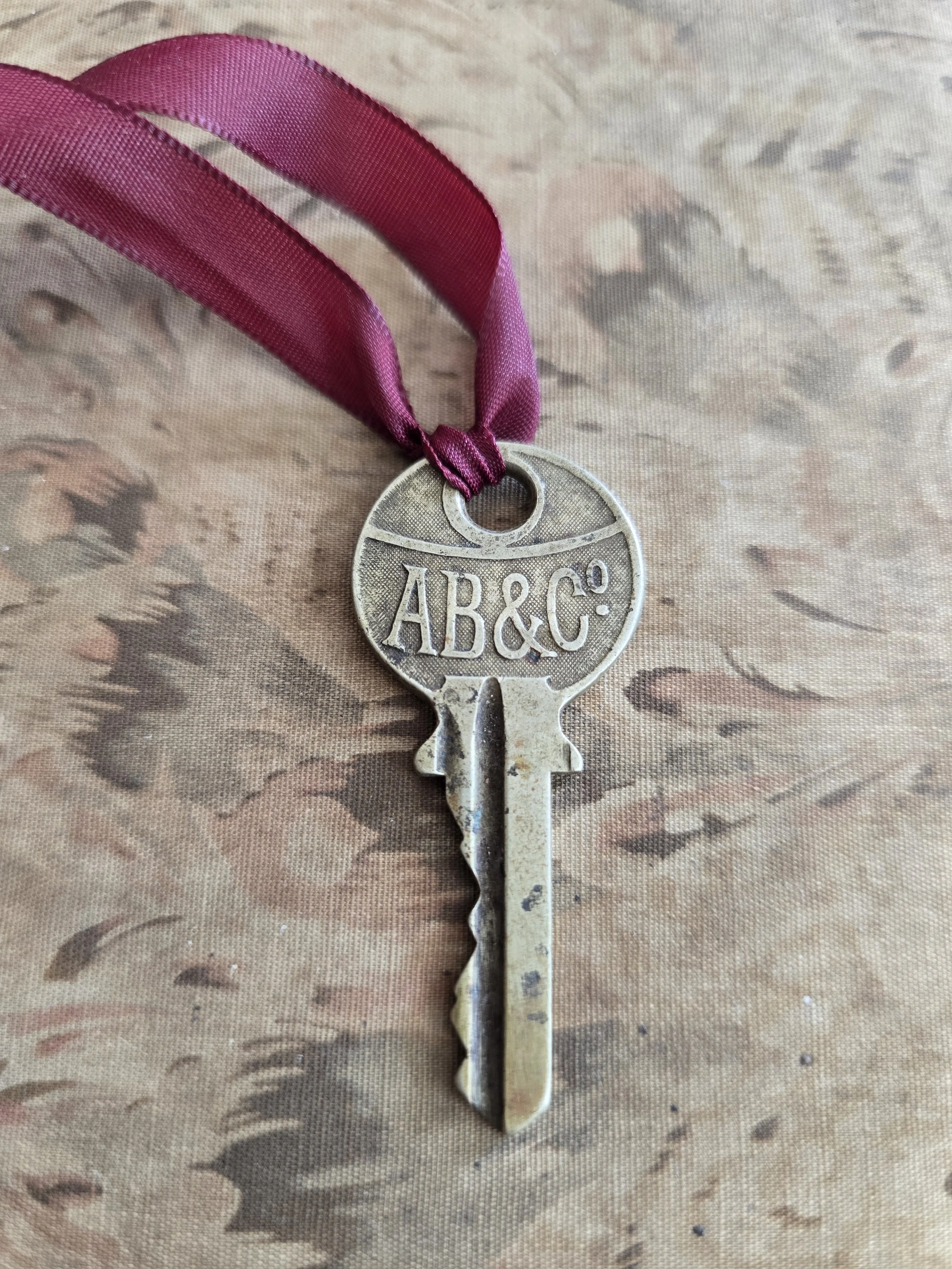 Vintage AB&C key with burgundy ribbon on floral textile background